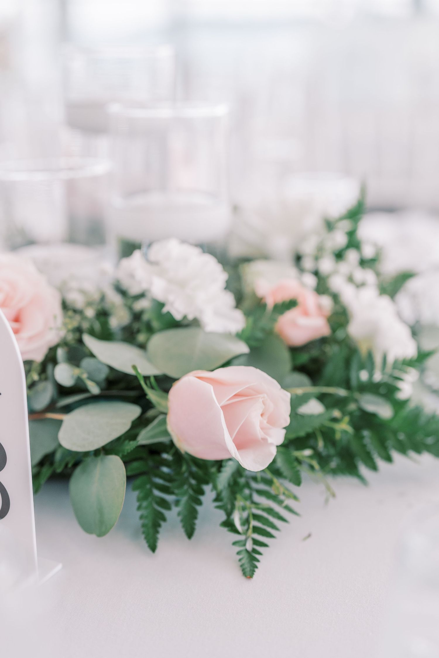 Delicate pink roses and white flowers arranged with eucalyptus leaves in an elegant wedding table garland centerpiece.