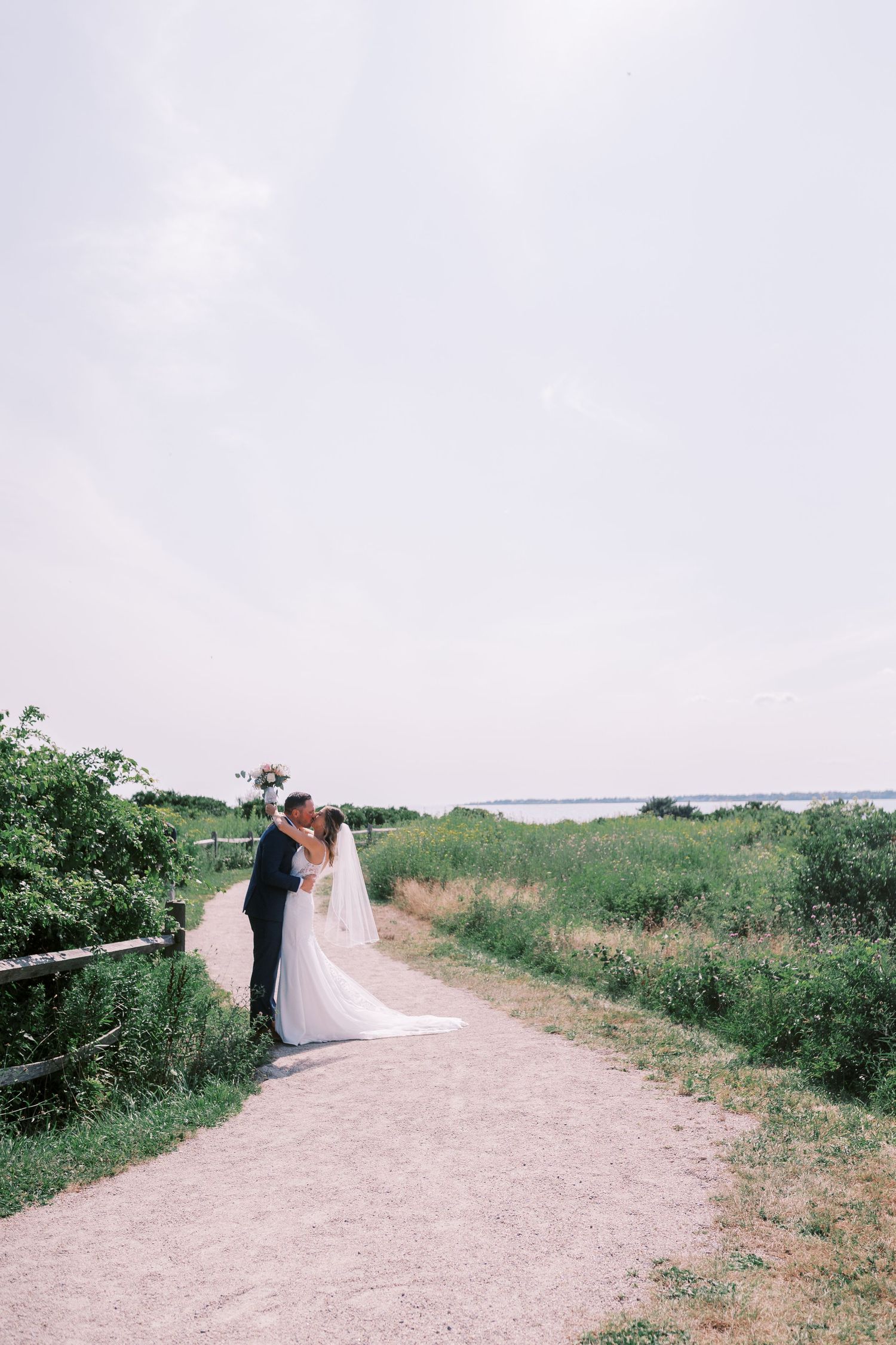 A couple shares an intimate moment on a coastal path surrounded by green foliage and ocean views.