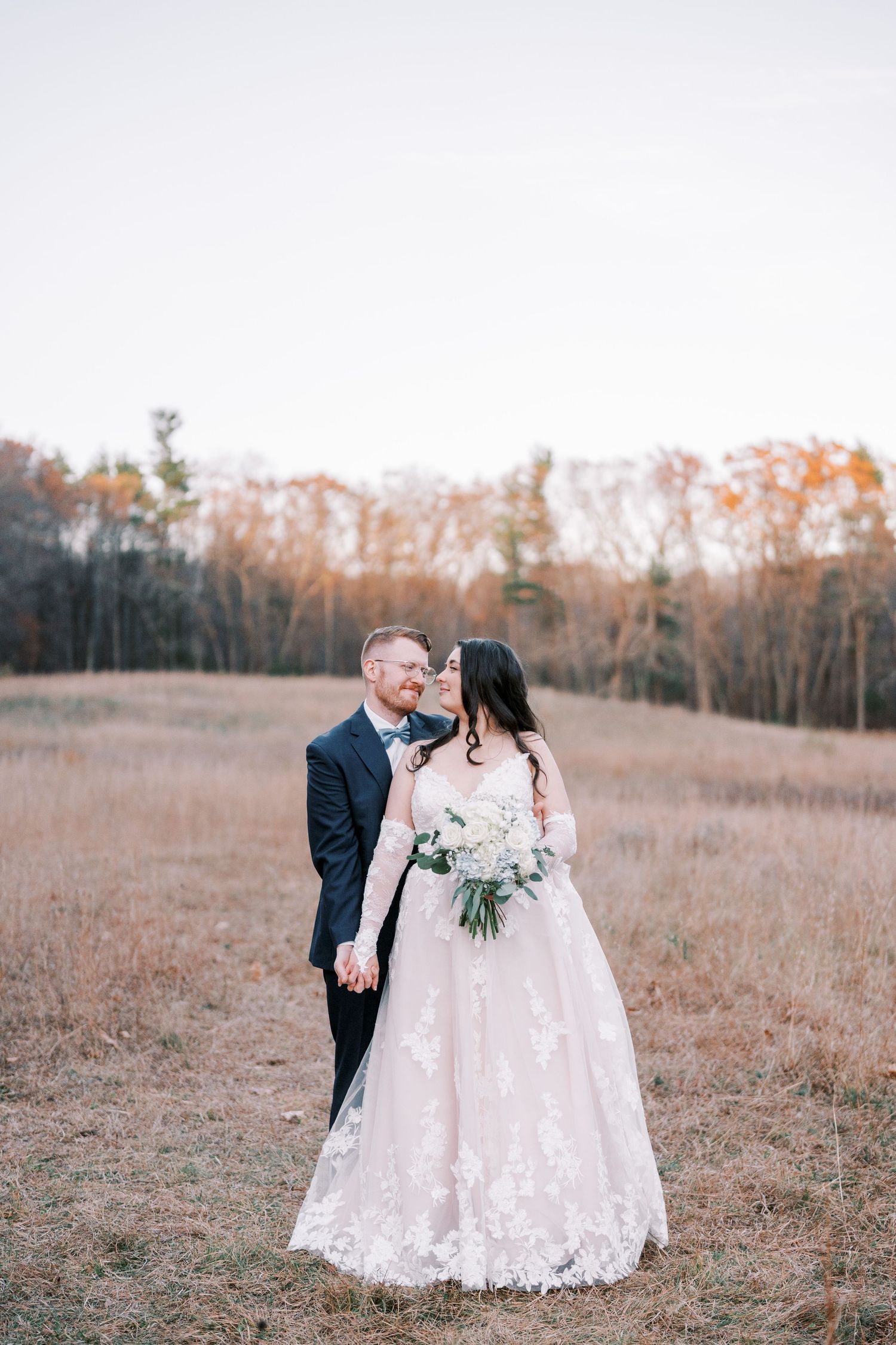 A couple shares an intimate moment in a rustic autumn field with golden foliage in the background.