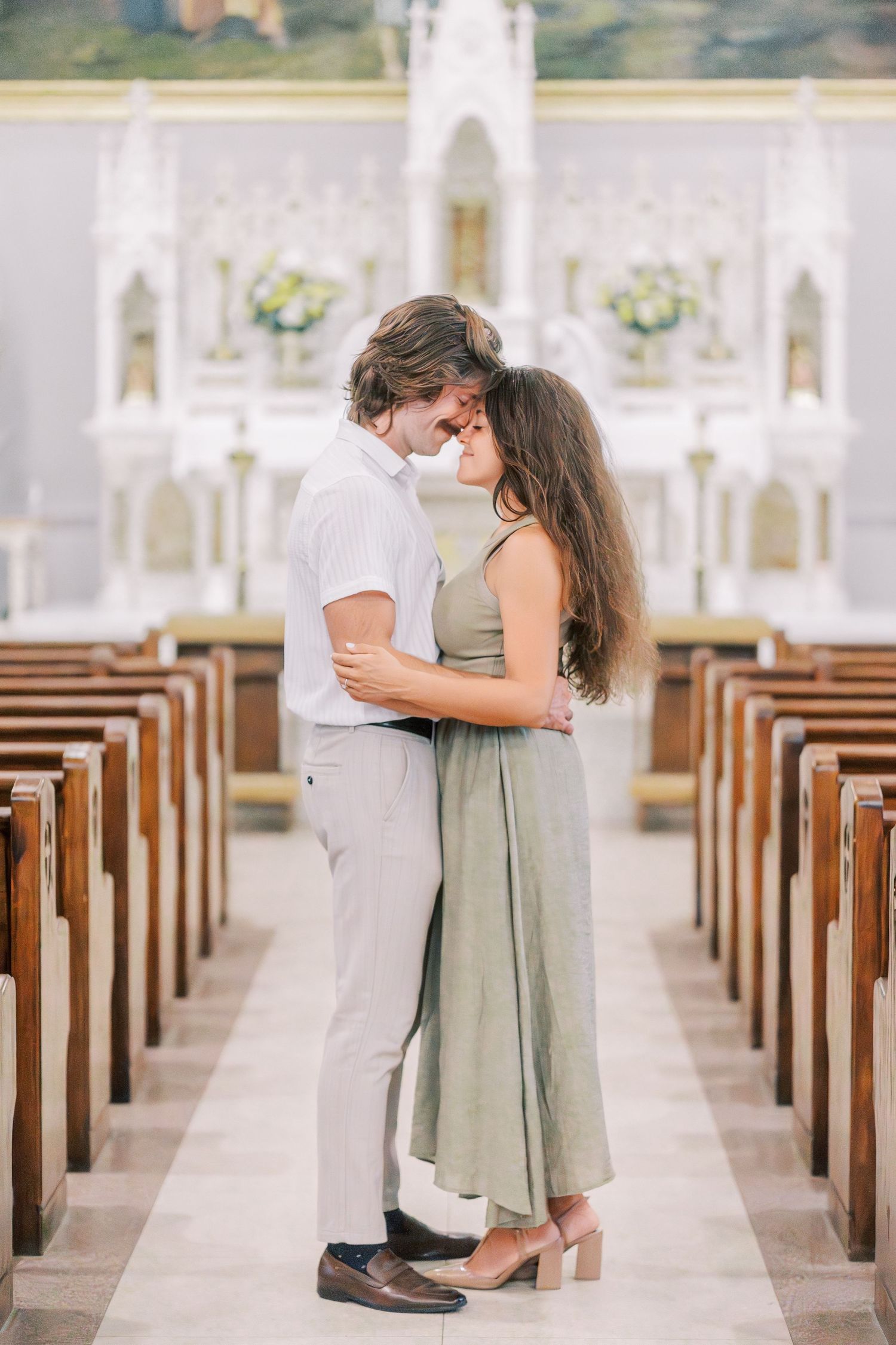 A couple shares an intimate moment in a sunlit church aisle with wooden pews.