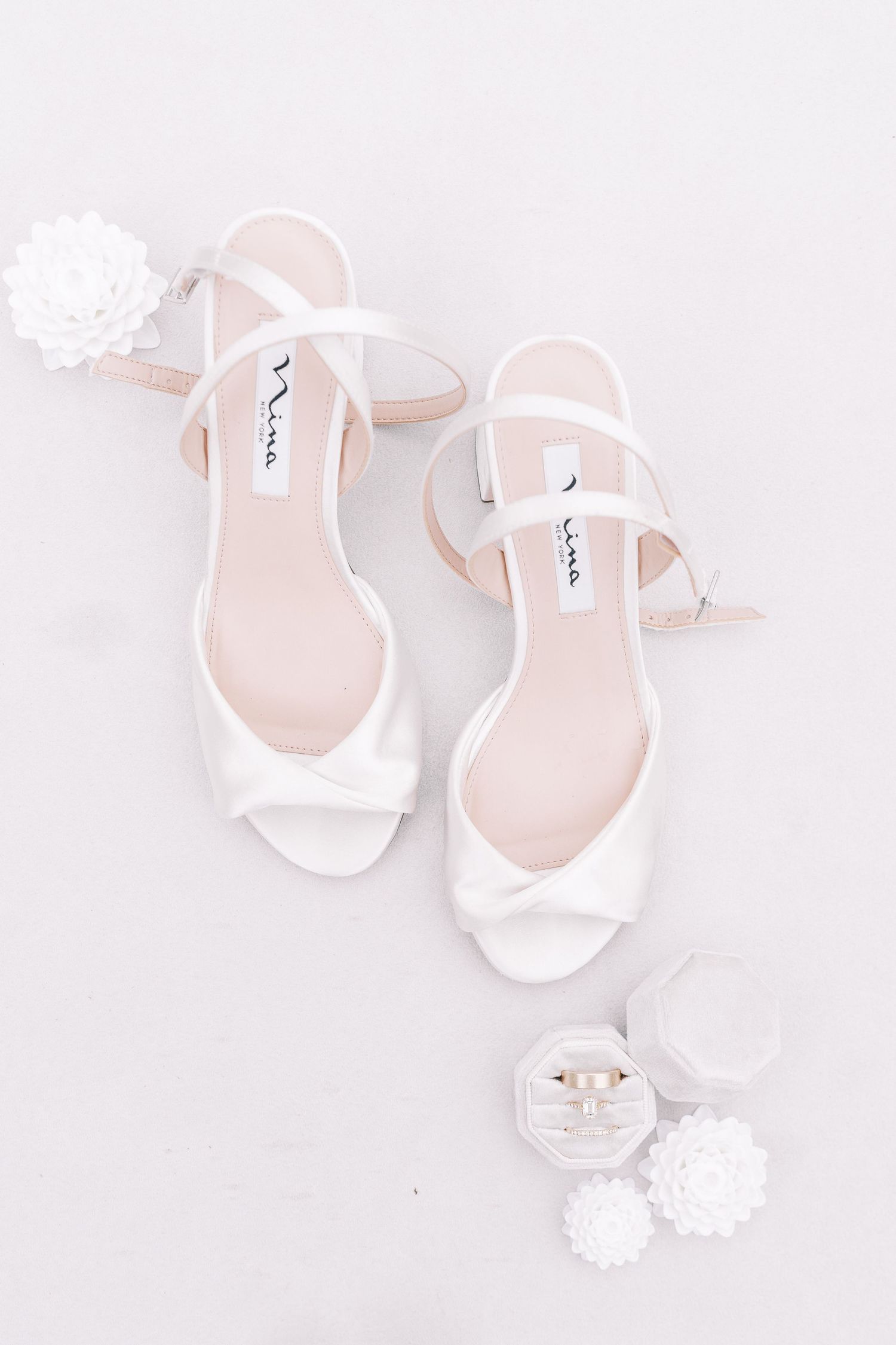 Elegant white bridal sandals with pom pom accessories on a light gray background.