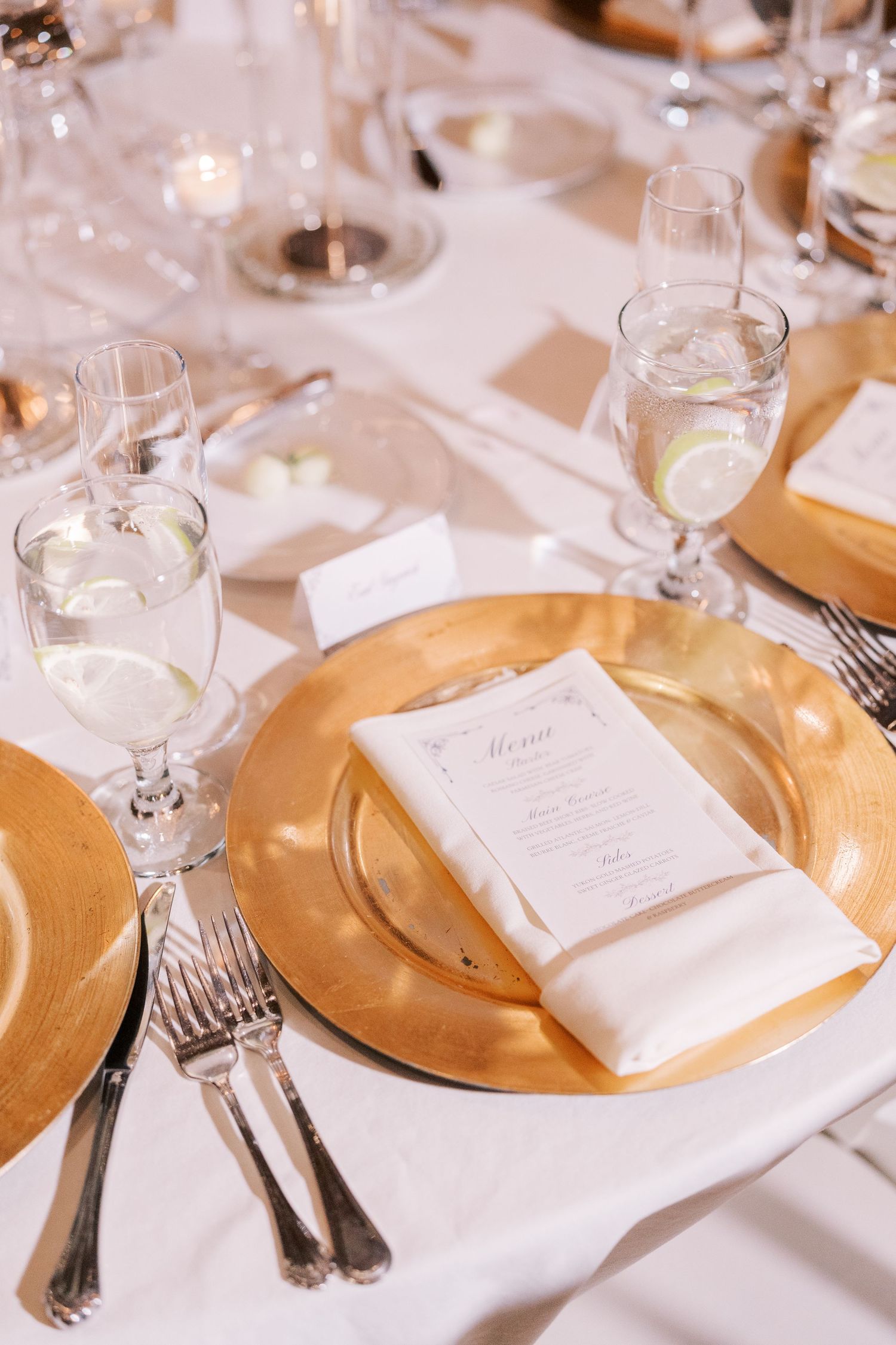 Elegant table settings with gold charger plates, white linens, and crystal glassware at a formal dining event.