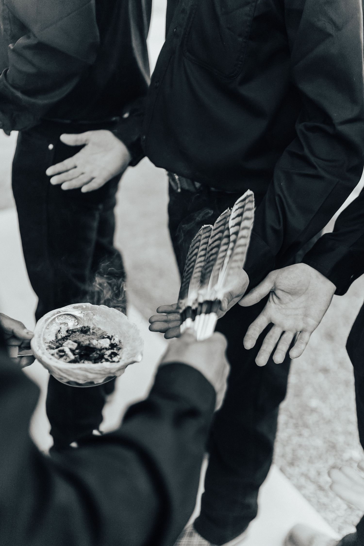 Black and white photo of hands performing a Native American smudging ceremony with feathers and burning herbs.