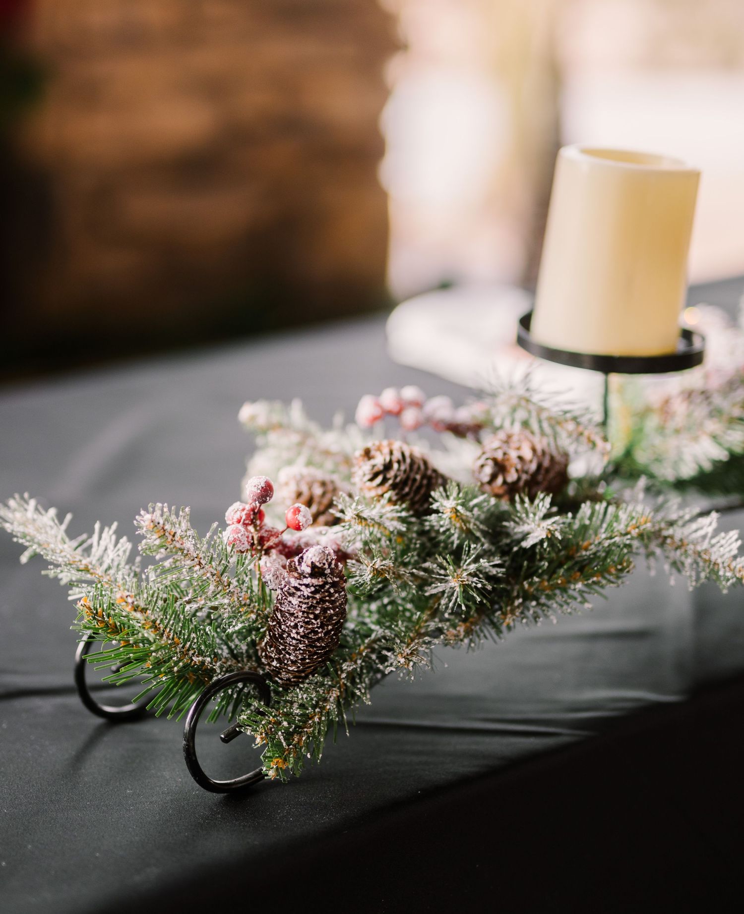 A festive holiday table arrangement with frosted pine branches, pink flowers and a white candle in a metallic holder.