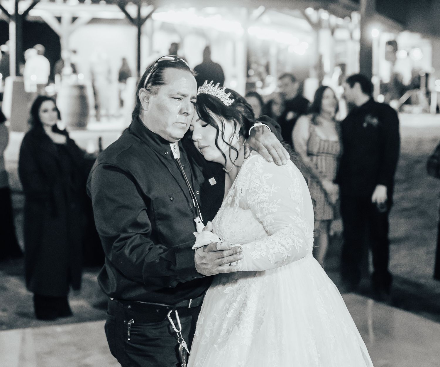 A couple shares a tender moment in black and white during their winter wedding ceremony with spectators in background.