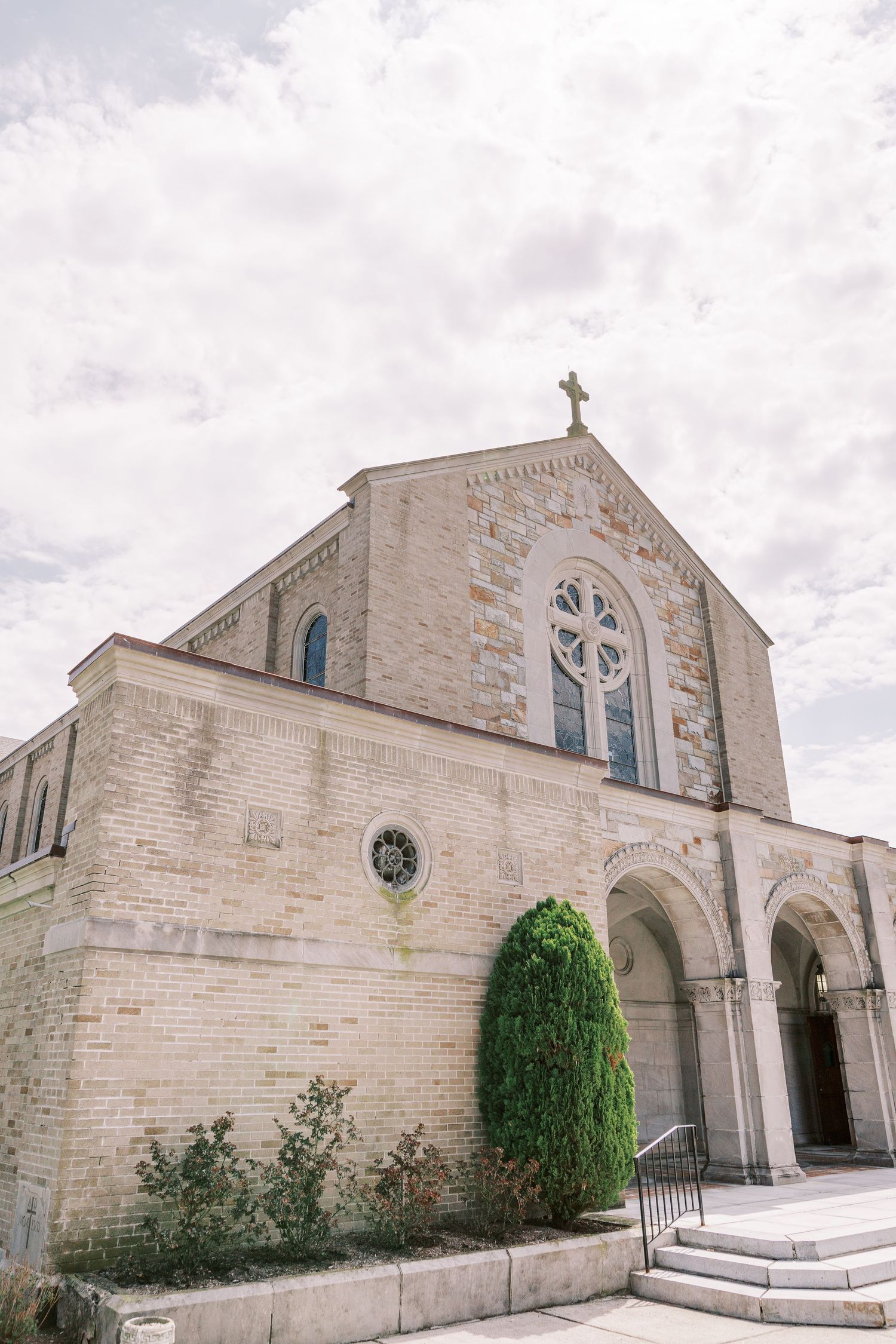 Stone church exterior with Gothic architecture features and arched entrances under cloudy skies.
