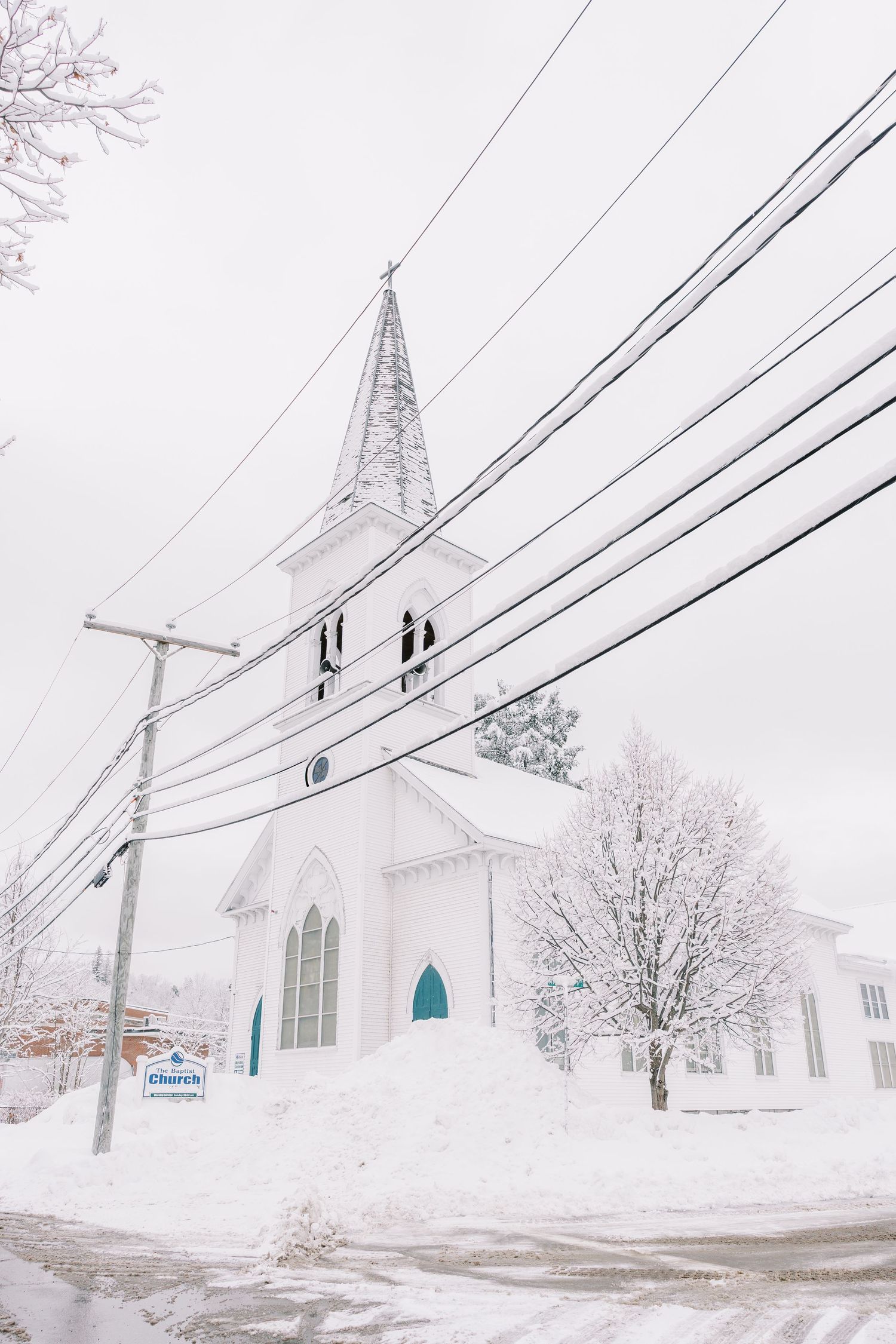 A series of white church buildings in a snowy winter landscape with power lines visible against the grey sky.