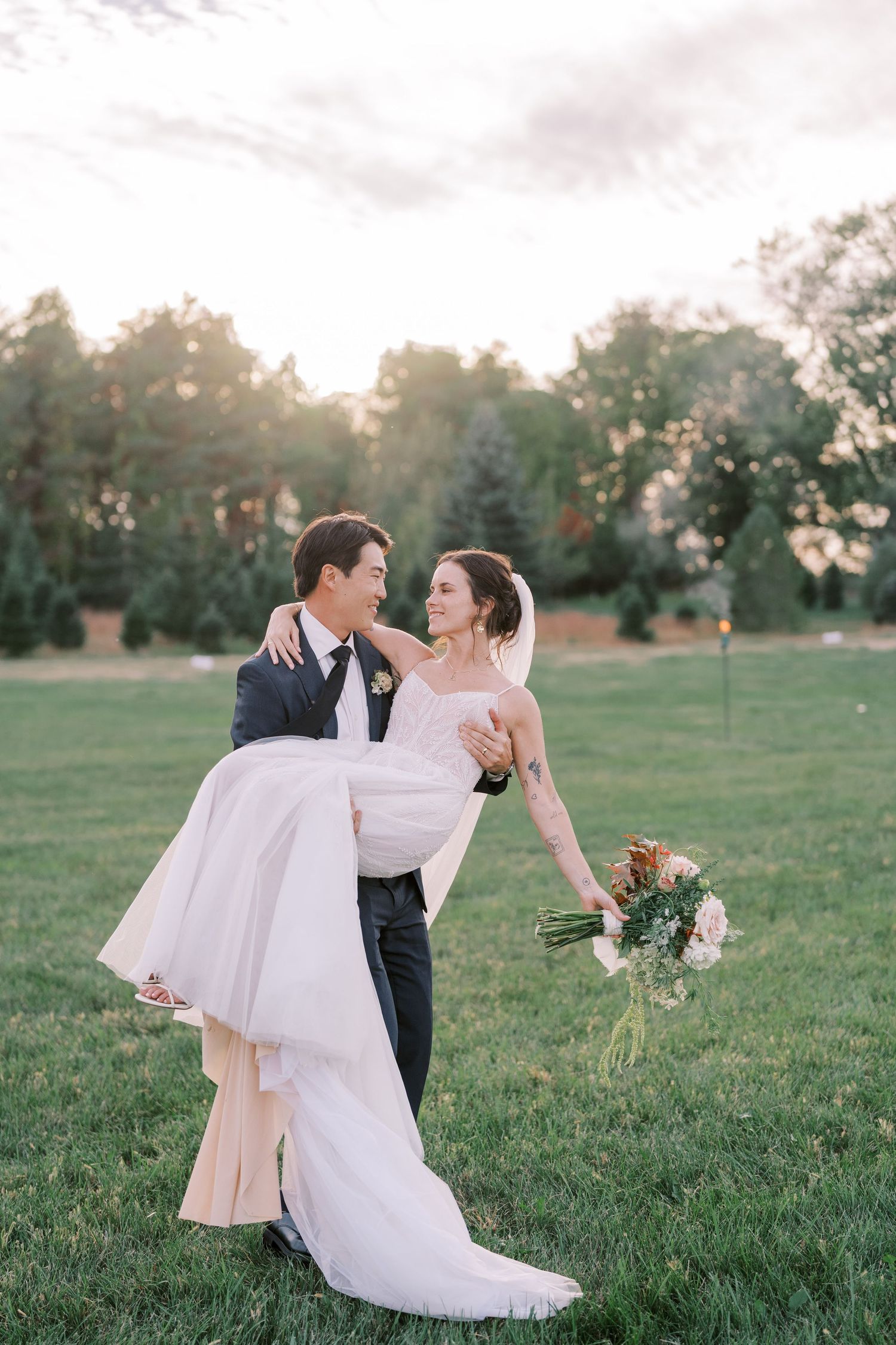 Romantic wedding couple dancing and twirling on a grassy field during golden hour.