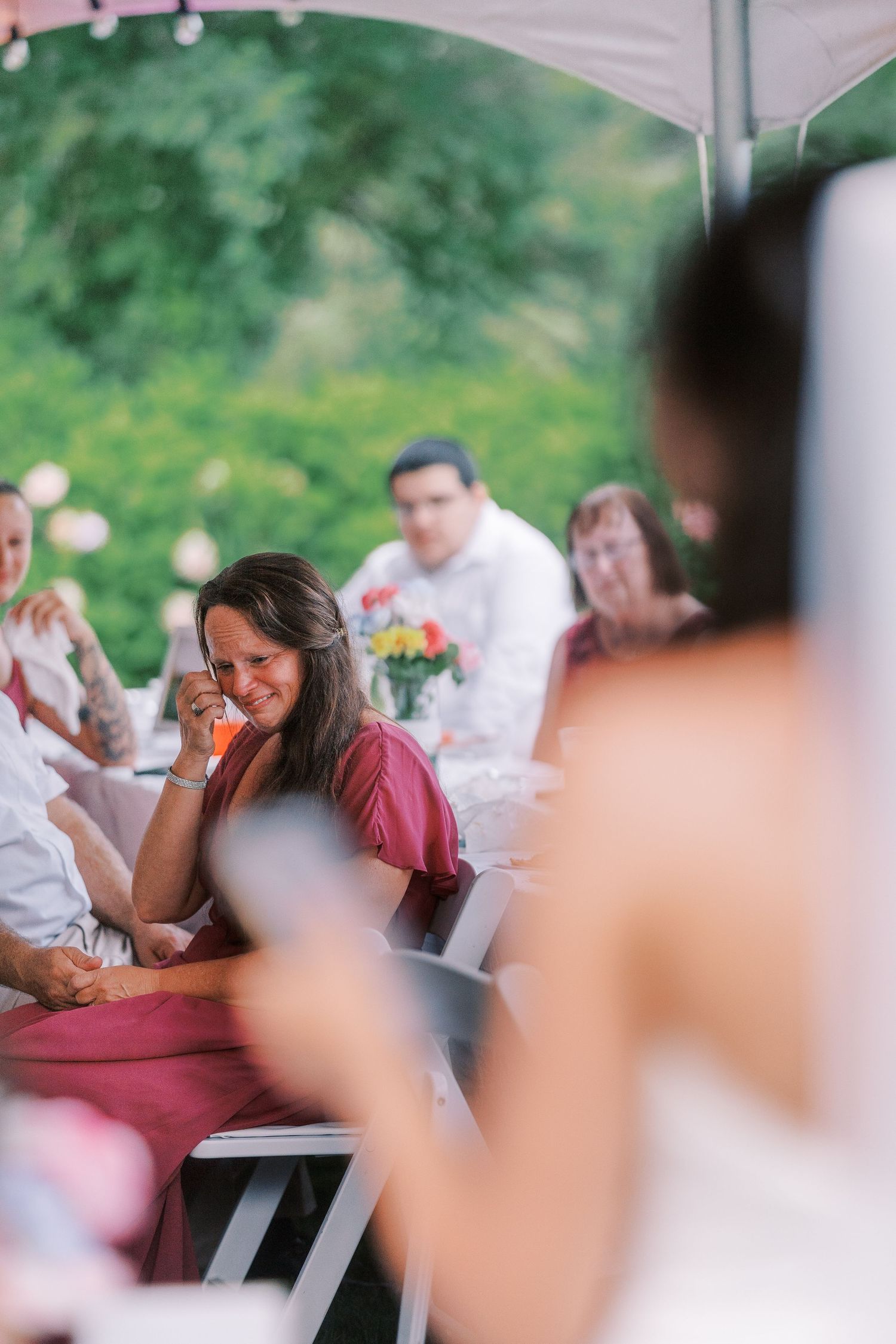 Wedding reception guests share joyful moments under a white tent with pink string lights.