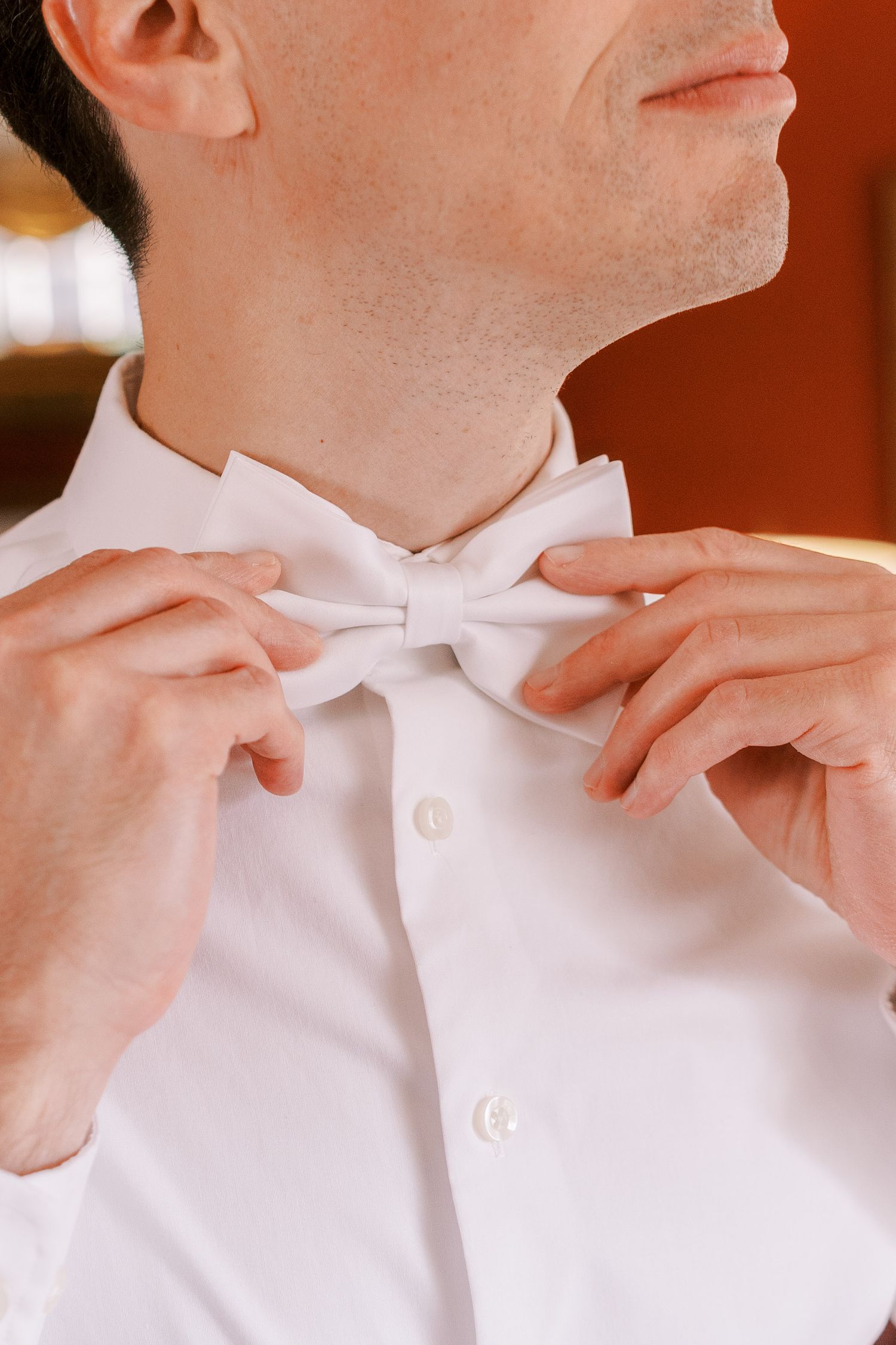 Close up of hands adjusting a white bow tie on formal attire.