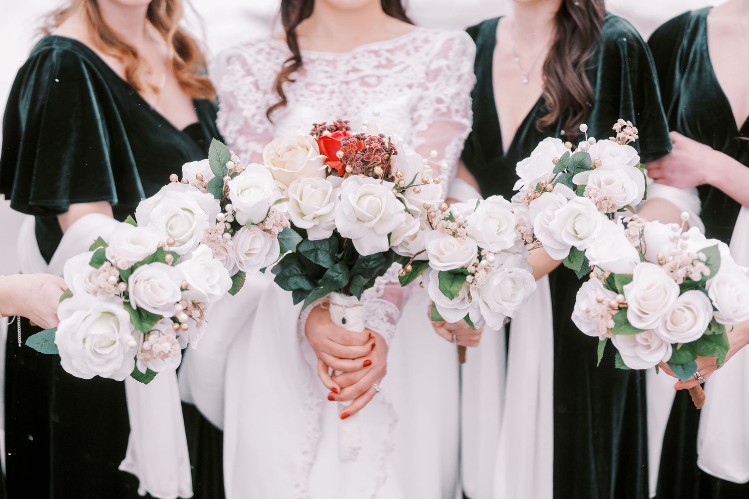 Bridesmaids in black dresses hold white bouquets while standing in a snowy winter setting.