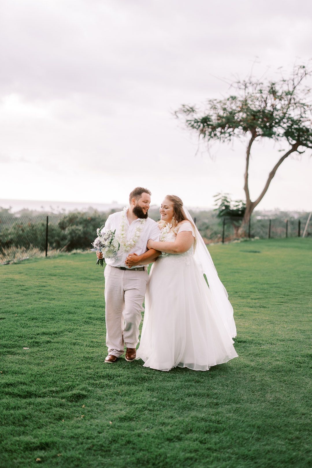 A romantic wedding couple shares a sweet moment together on a grassy hillside under a lone tree.