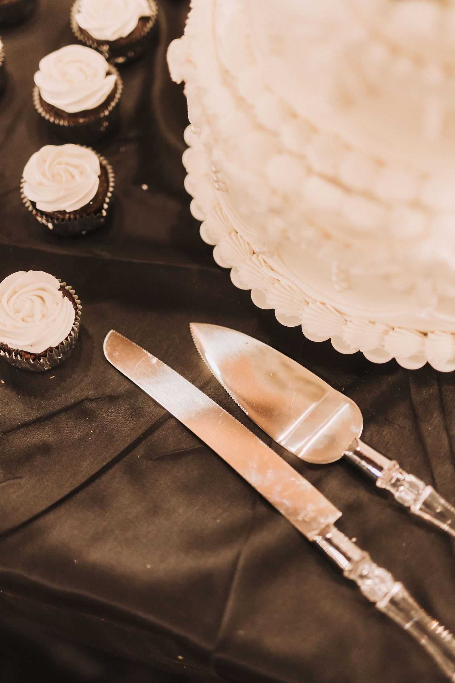 A vintage-style sepia photograph showing cake serving utensils and cupcakes with frosting on a dark tablecloth.