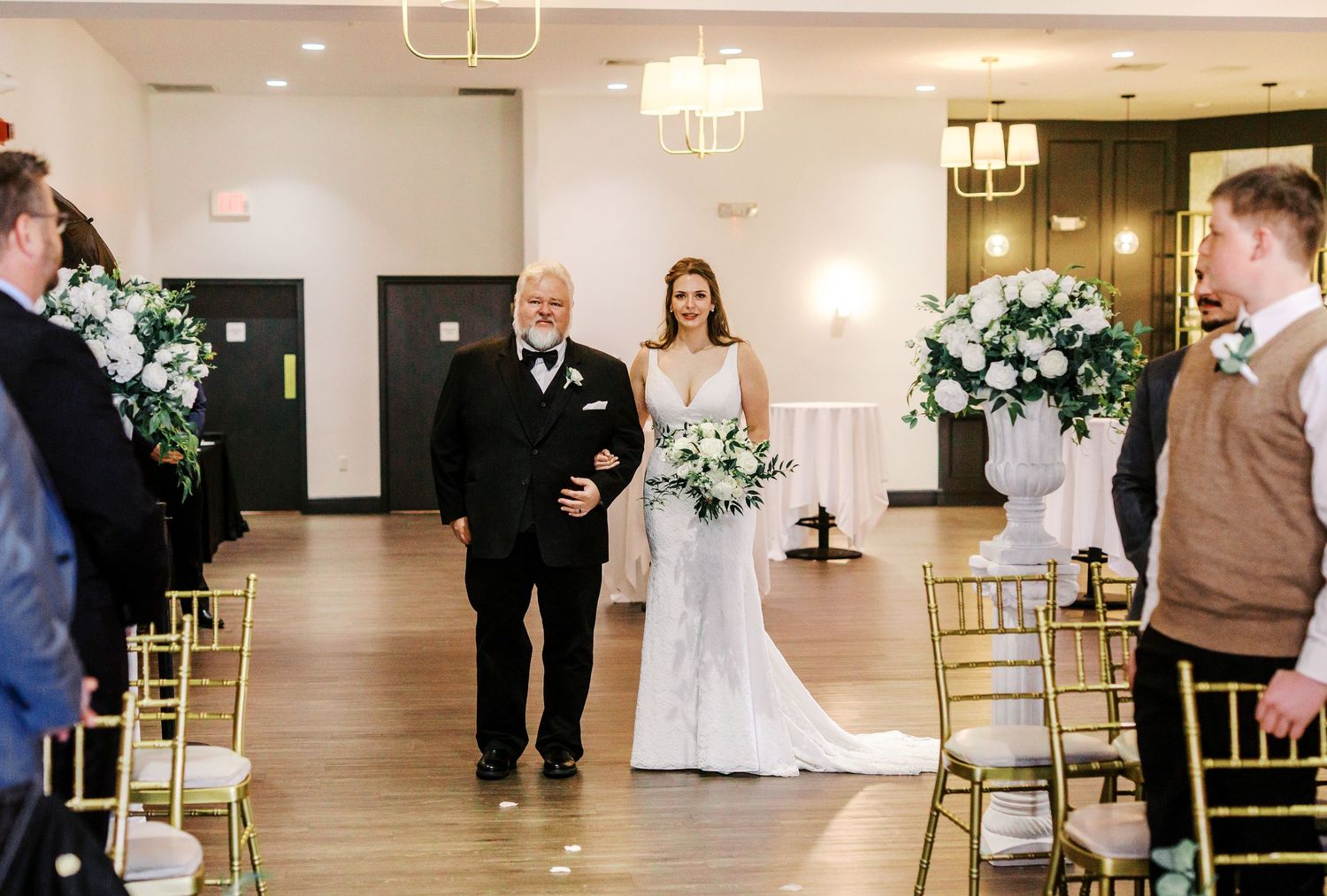 Wedding ceremony setup in an elegant indoor venue with white decor and gold chiavari chairs.