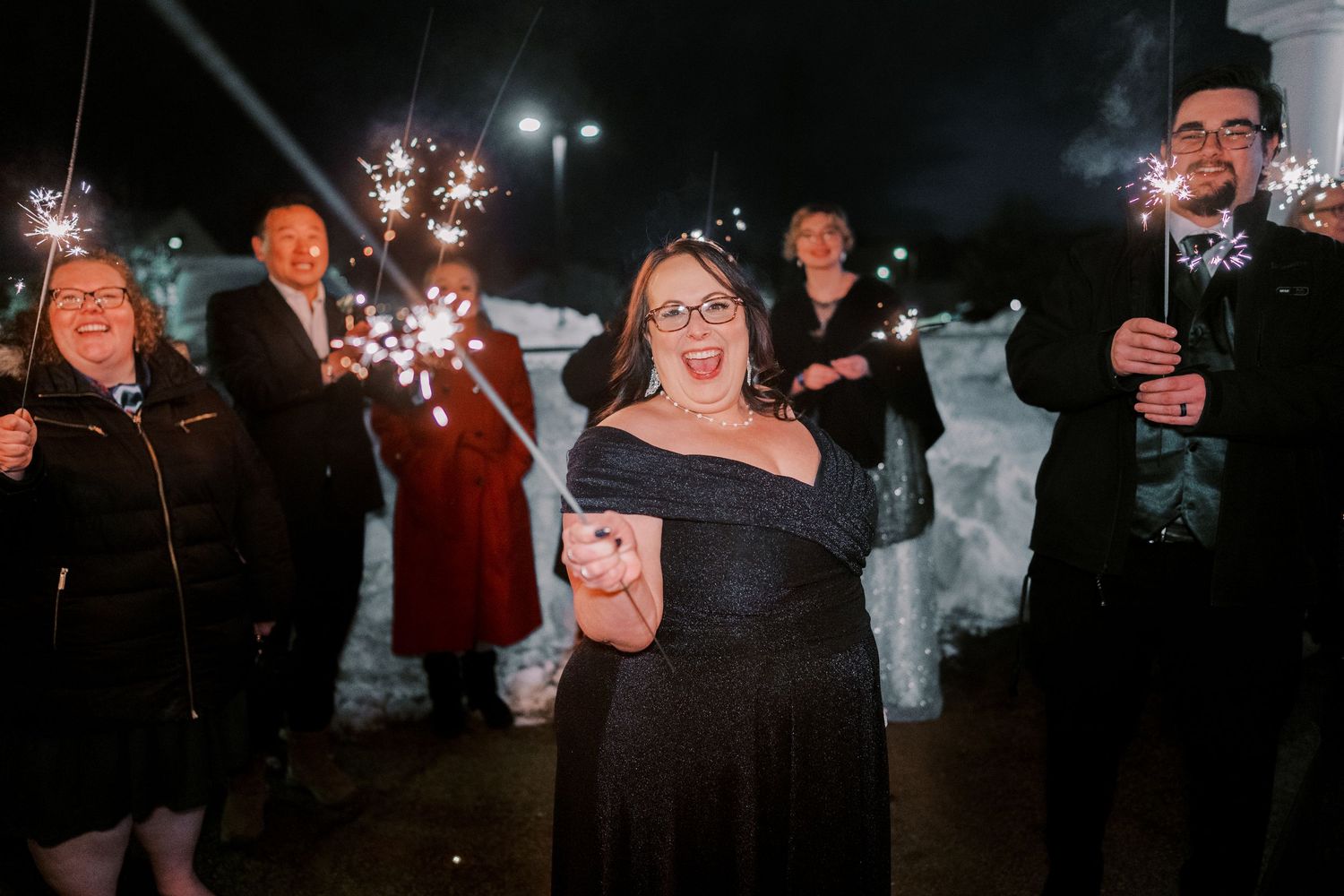 Wedding guests celebrate with sparklers during an outdoor nighttime celebration.