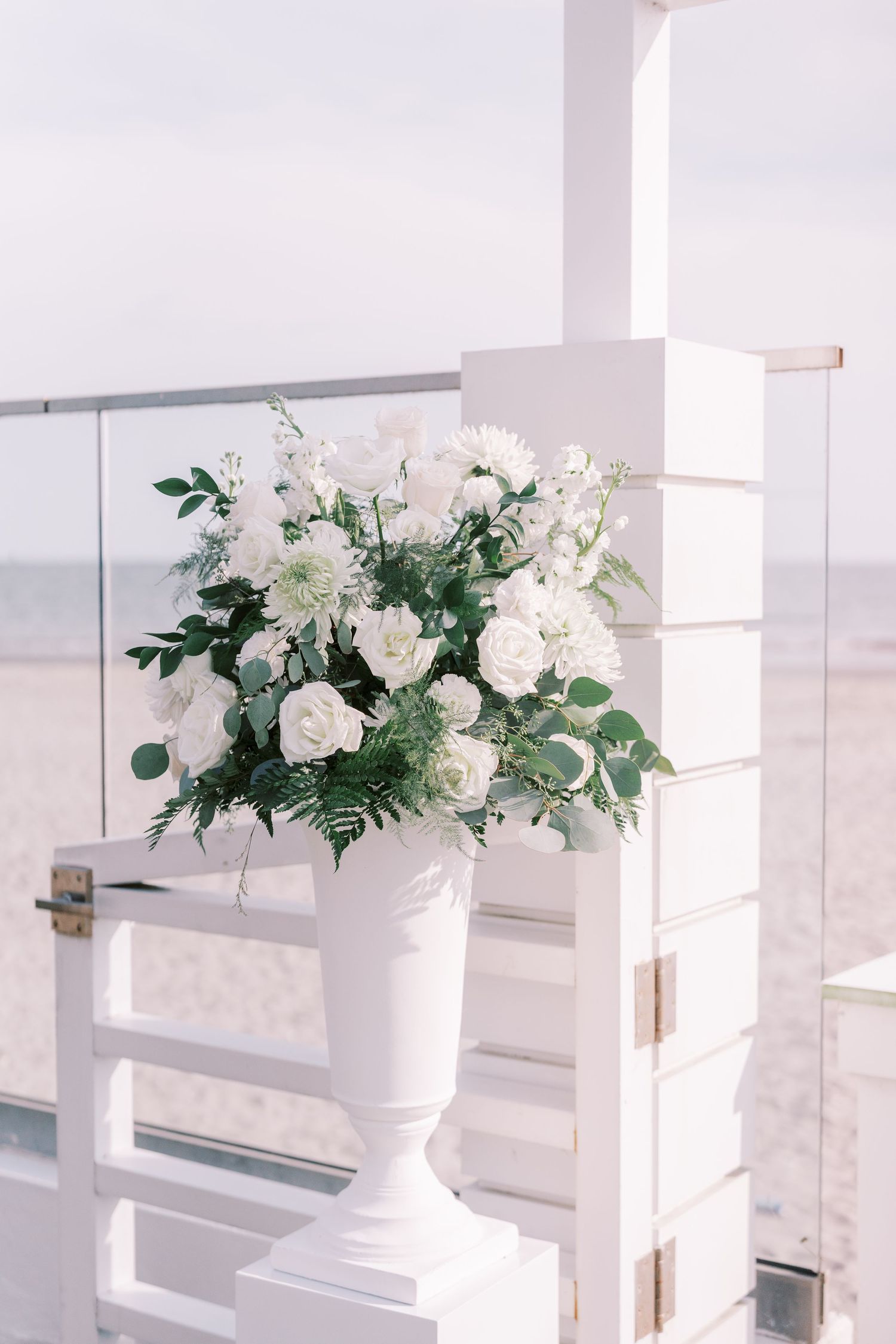 White floral arrangements in elegant urns displayed along a modern white railing with a bright, airy backdrop.