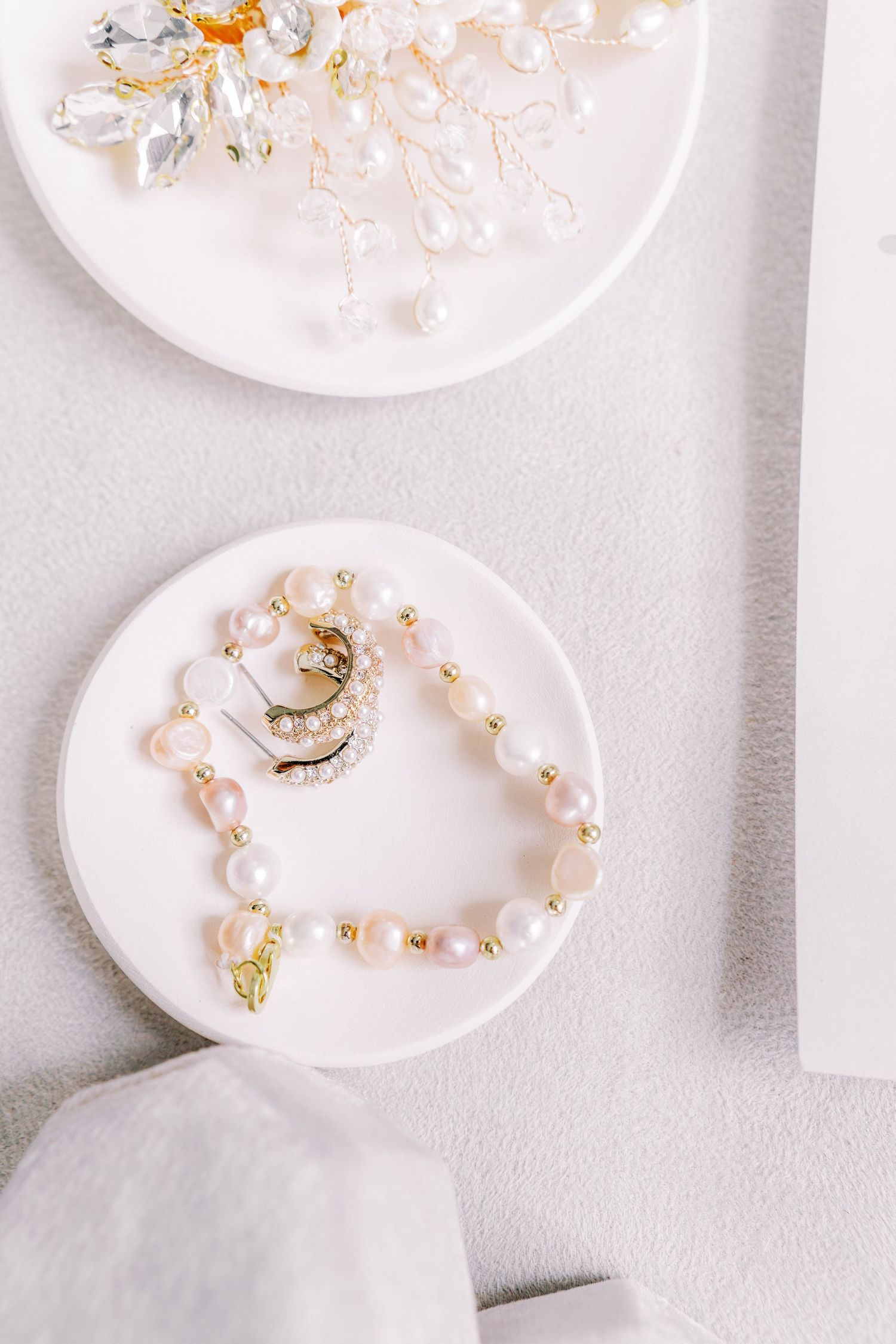 Delicate pearl jewelry and accessories displayed on white ceramic plates.