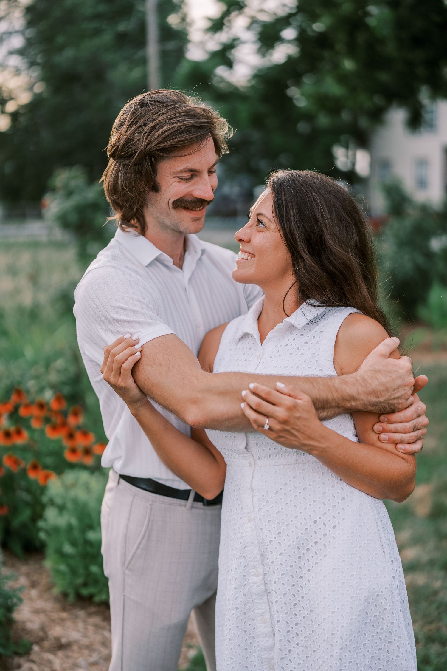 A couple dances and embraces in a garden with orange flowers blooming in the background.
