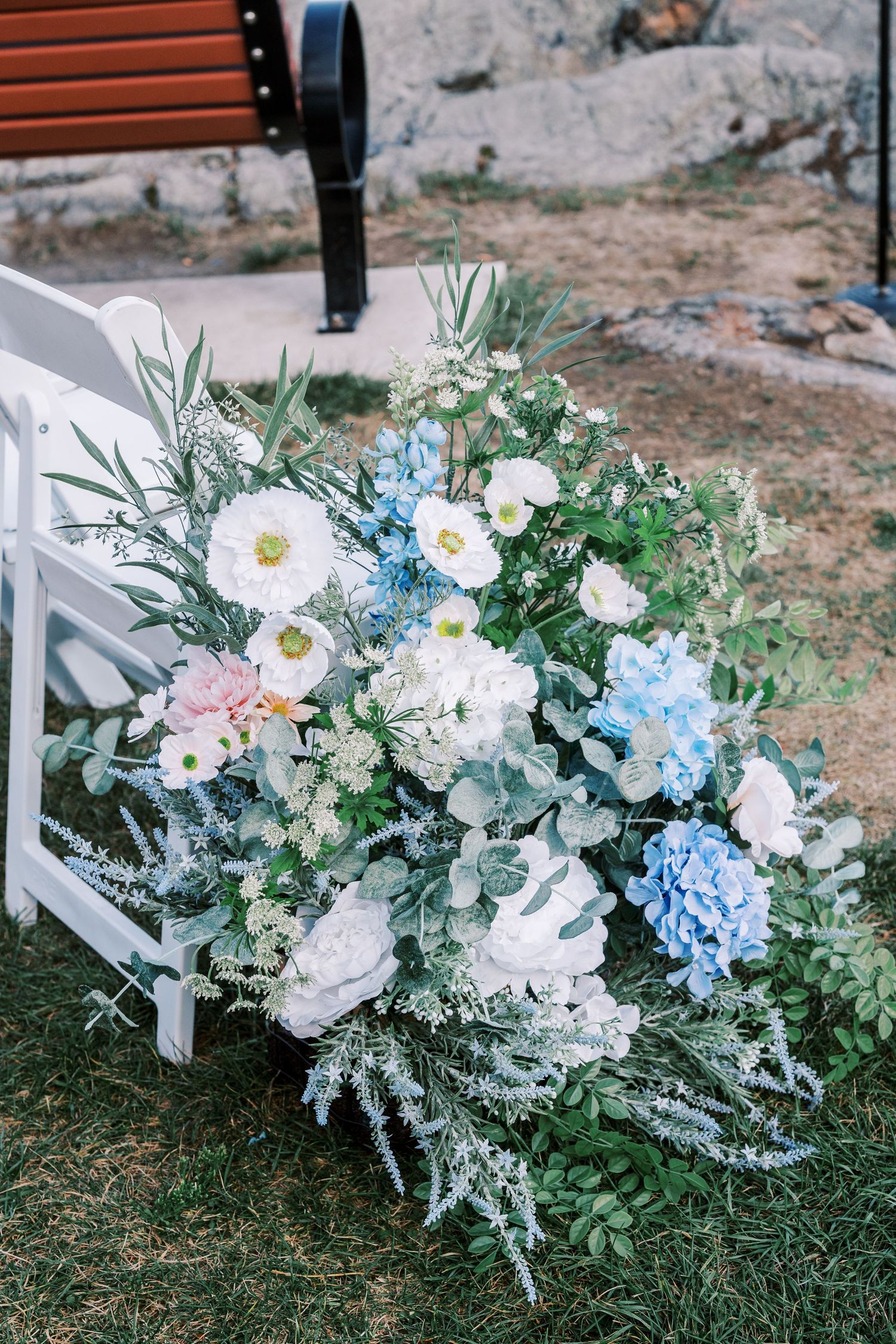 Romantic floral arrangement with white and blue flowers alongside greenery displayed near wooden seating.