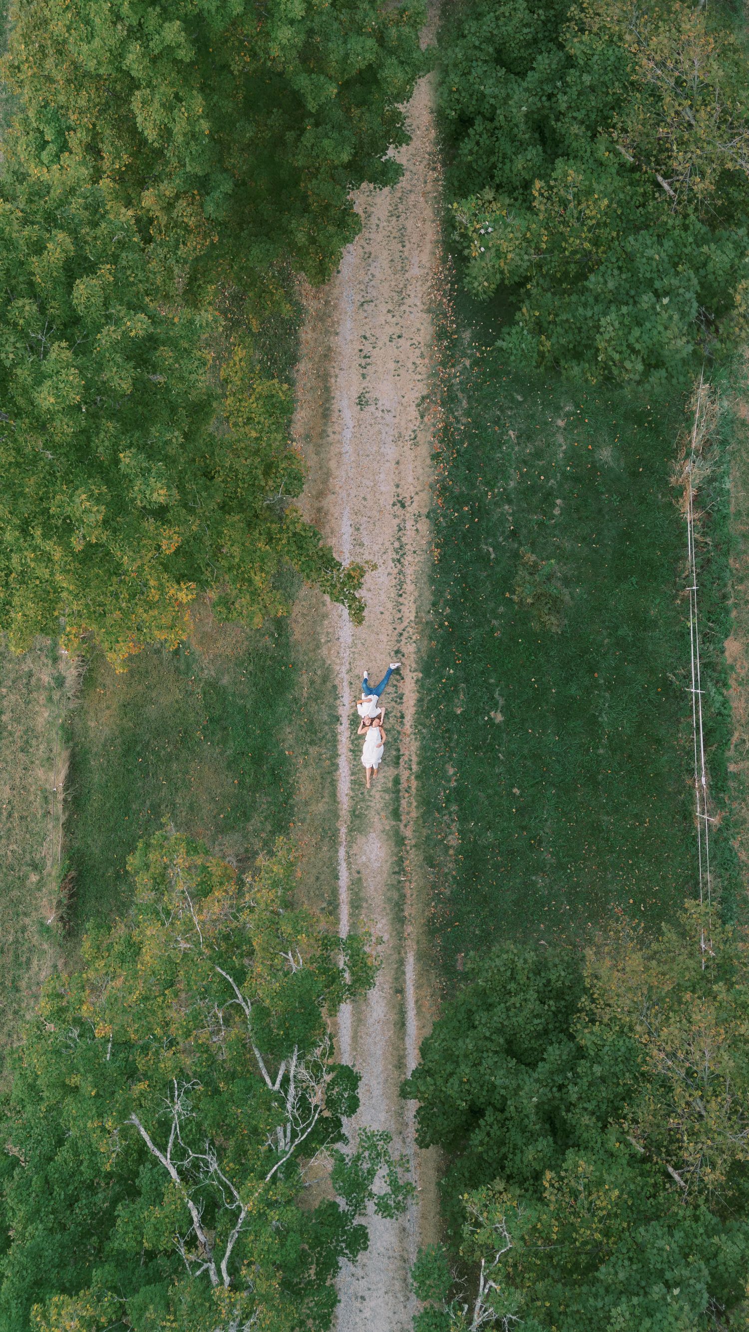 Aerial drone shot of a winding dirt path through lush green forest and vegetation.