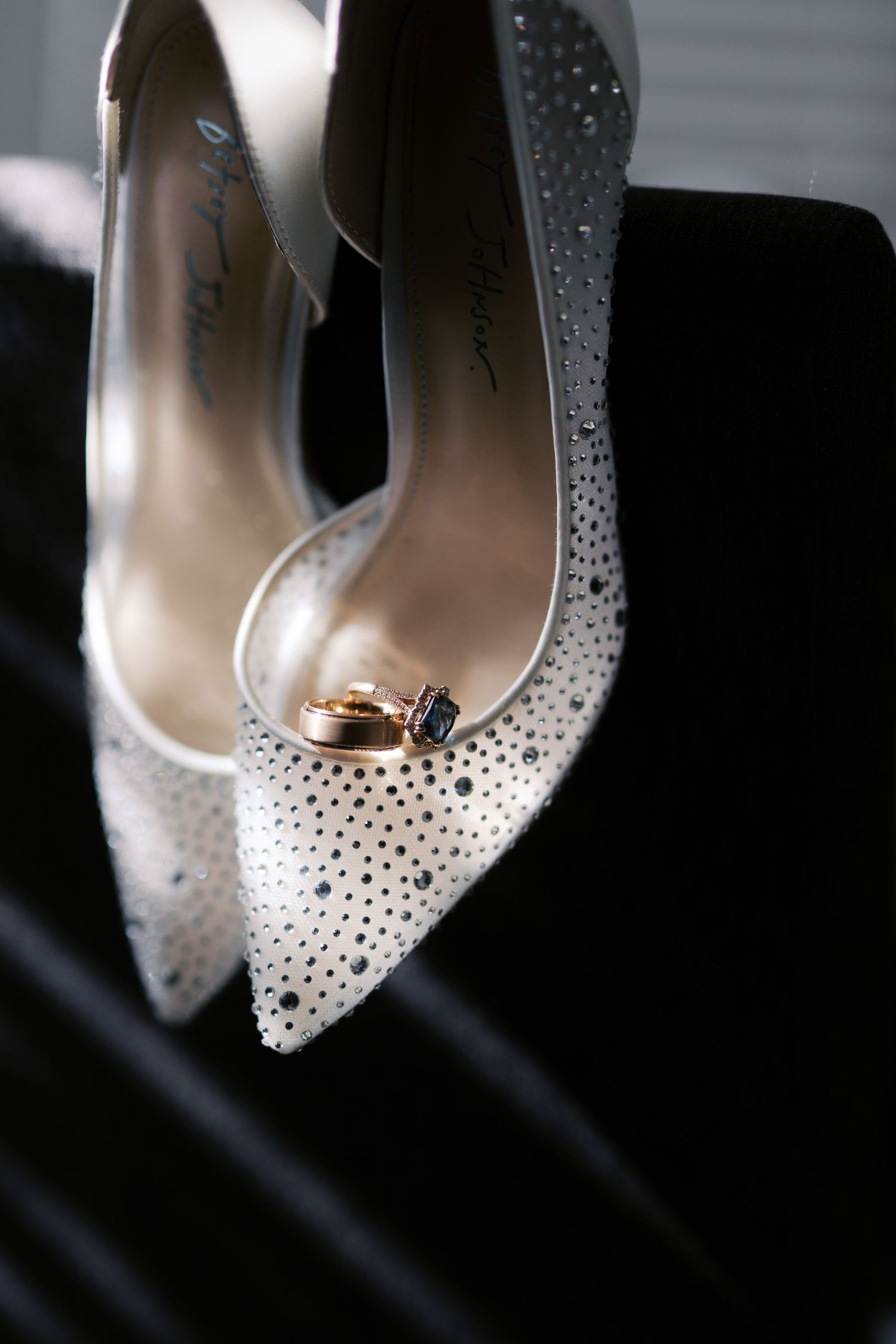 Elegant white bridal heels decorated with sparkly crystals with wedding rings placed inside the shoe.