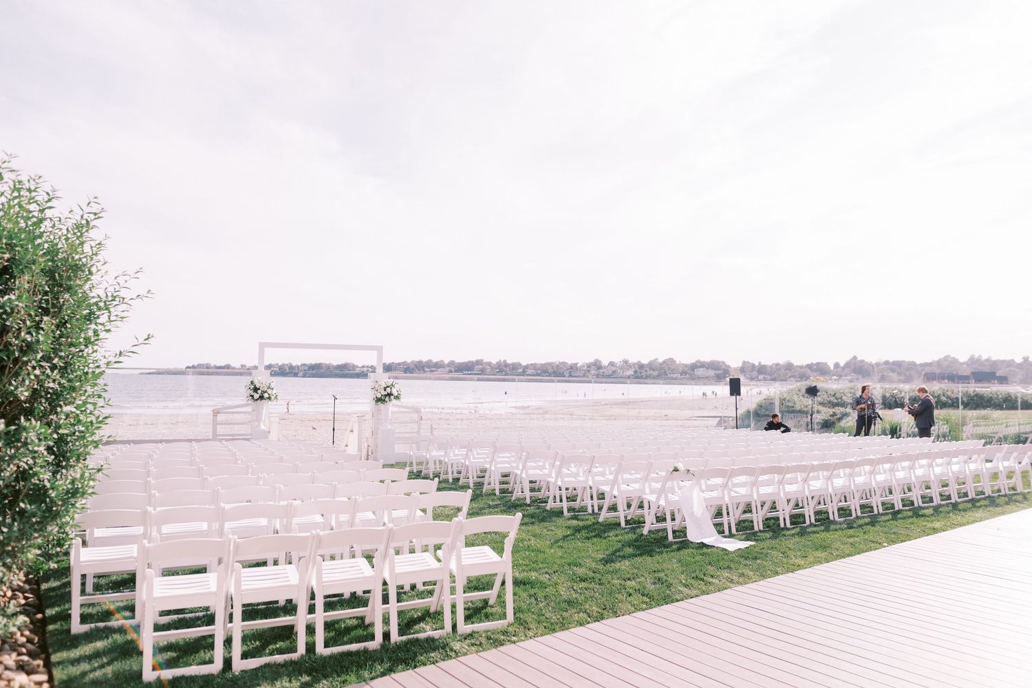 A panoramic view of white wooden chairs arranged in rows for an outdoor ceremony on a grassy lawn.