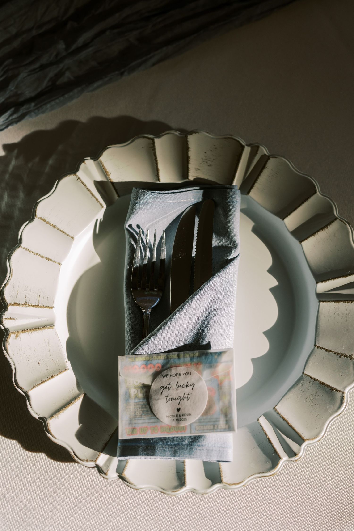 Elegant place setting with decorative white plate, black utensils and a small card in moody lighting.