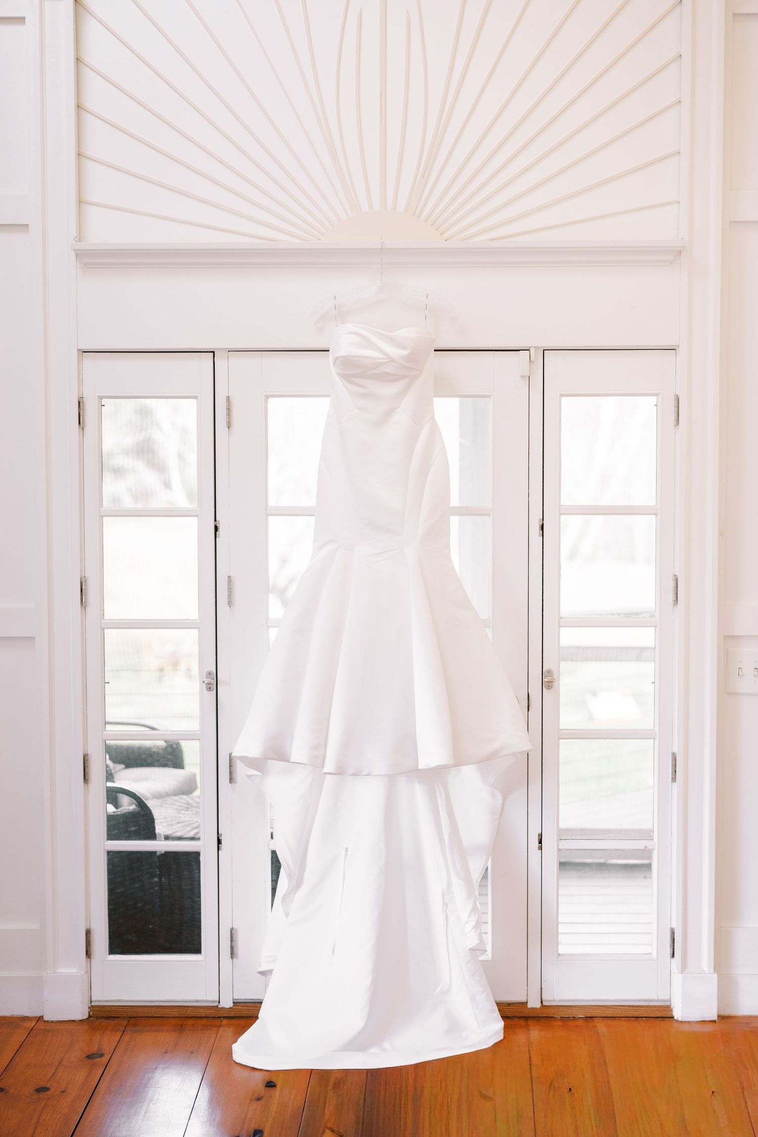 White curtains flow gracefully in front of sunlit windows with warm wooden flooring in a bright, minimalist interior.