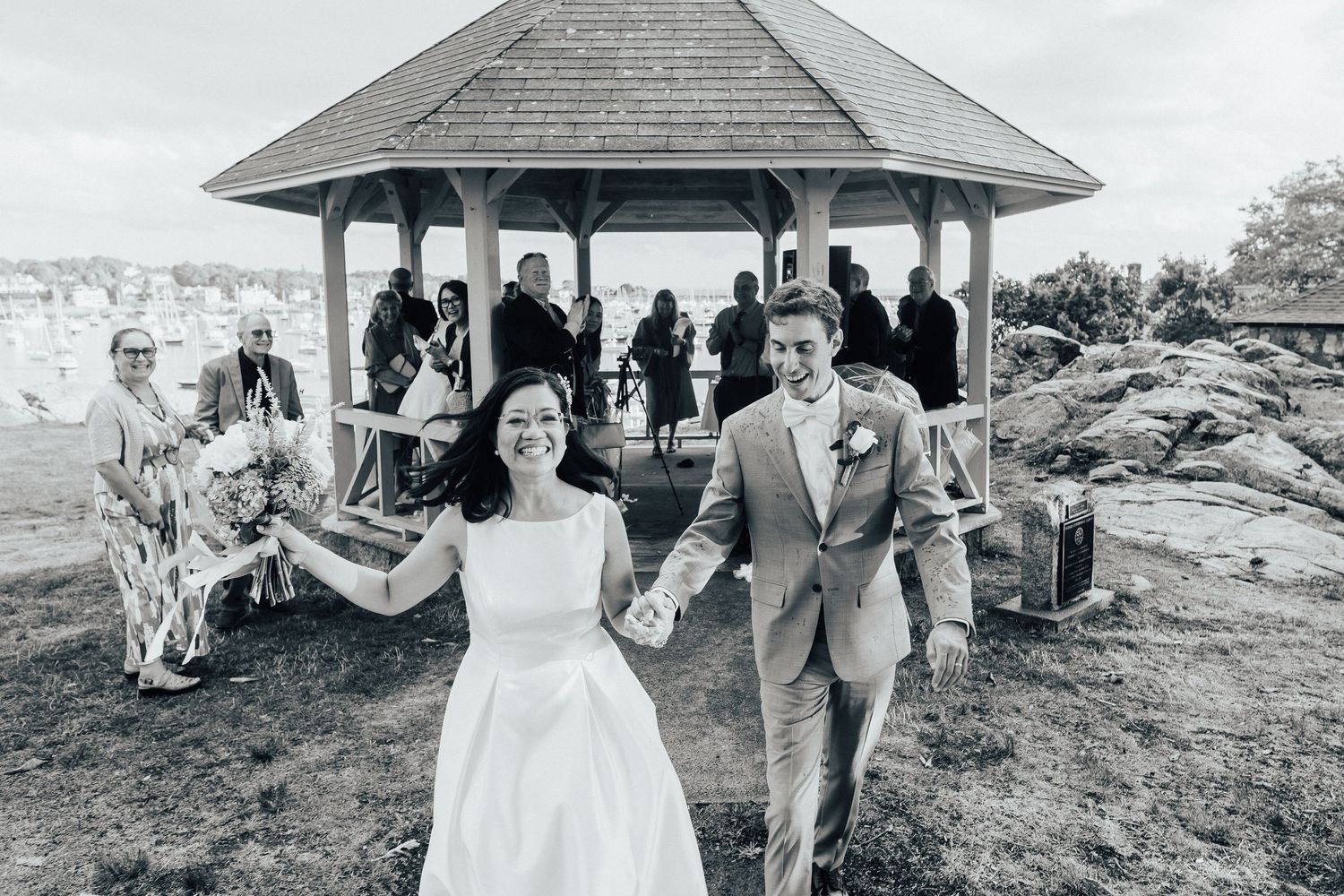 Rustic wedding venue with gazebo and people gathered around the scenic outdoor area.