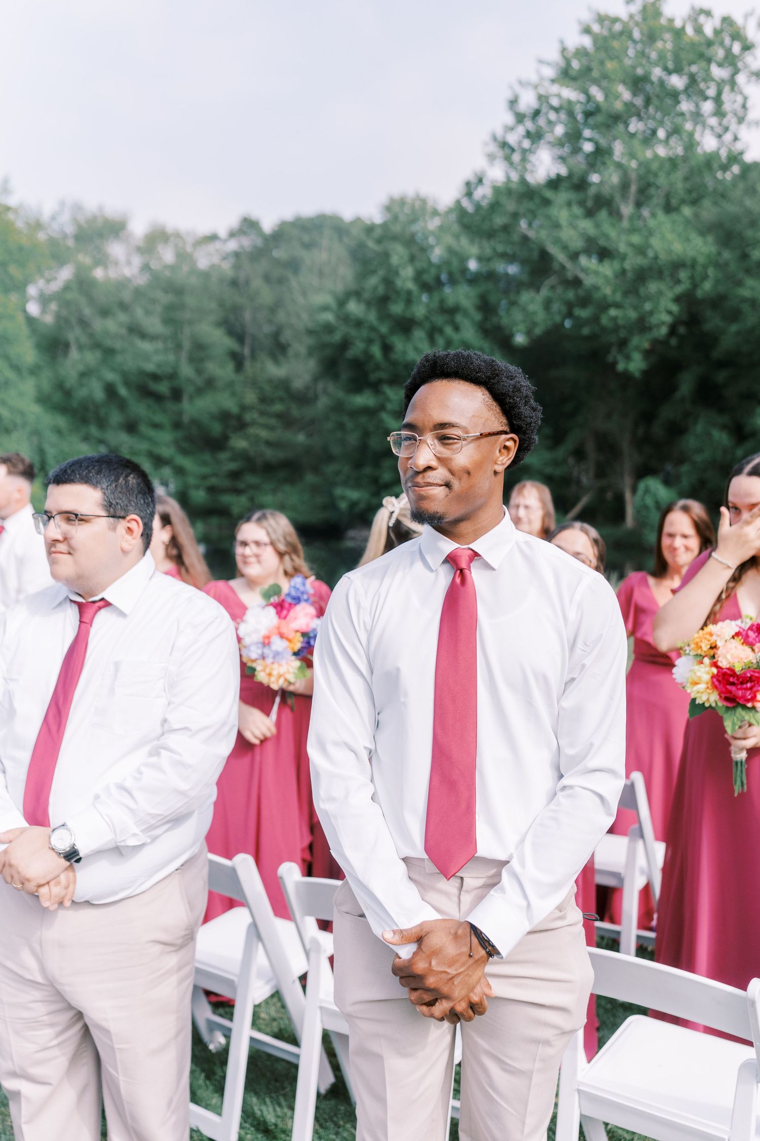 Groomsmen in pink ties and light colored suits standing at outdoor wedding ceremony.