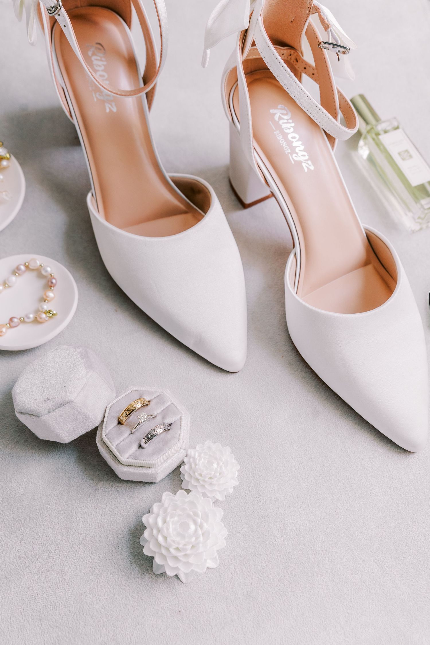 White bridal heels with floral accessories displayed on a light gray background.