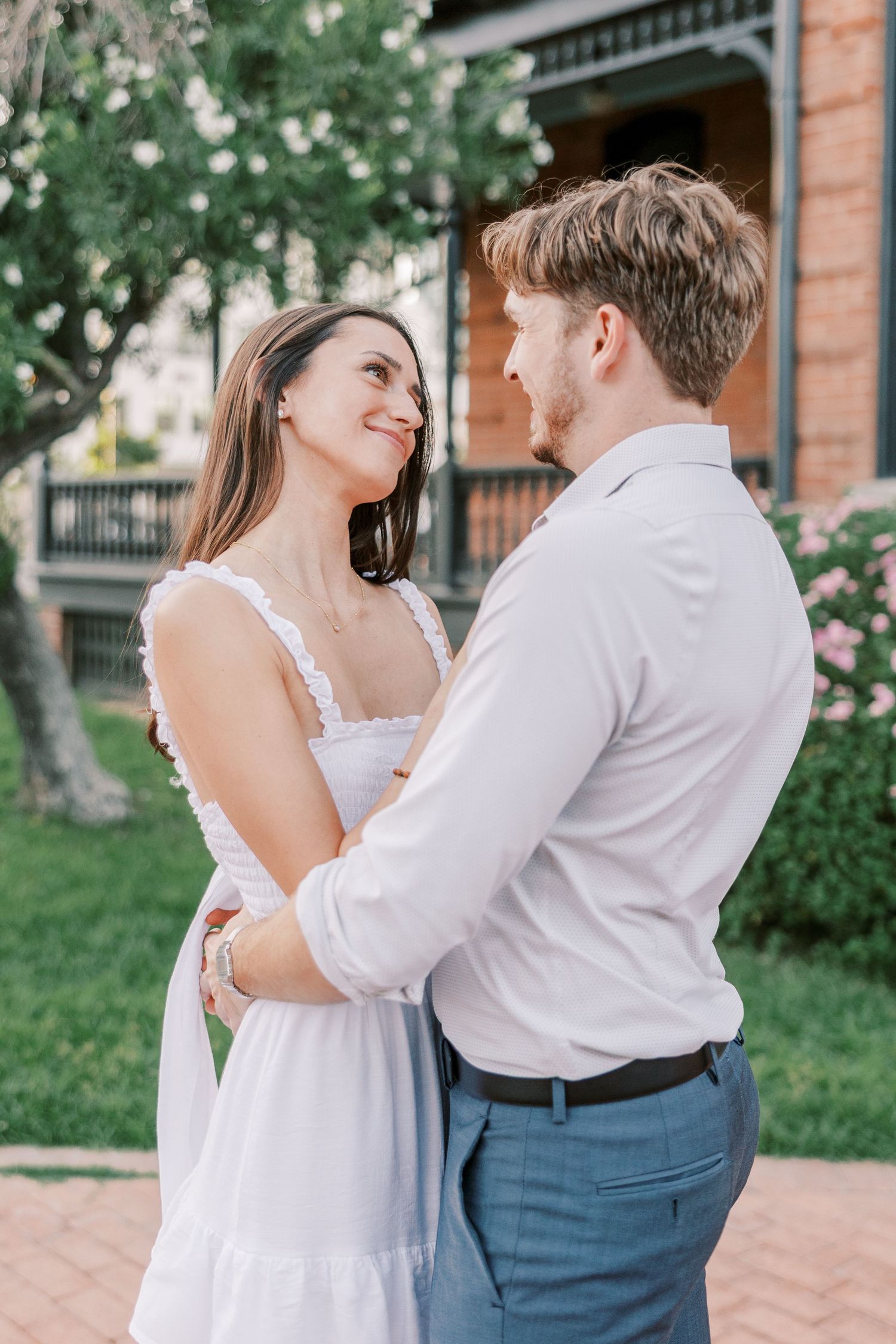 A couple shares an intimate moment while dancing outside a brick building with greenery.