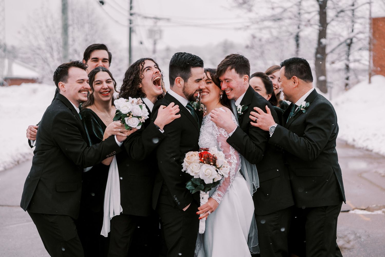 Wedding party laughs together while standing in the snow during a winter celebration.