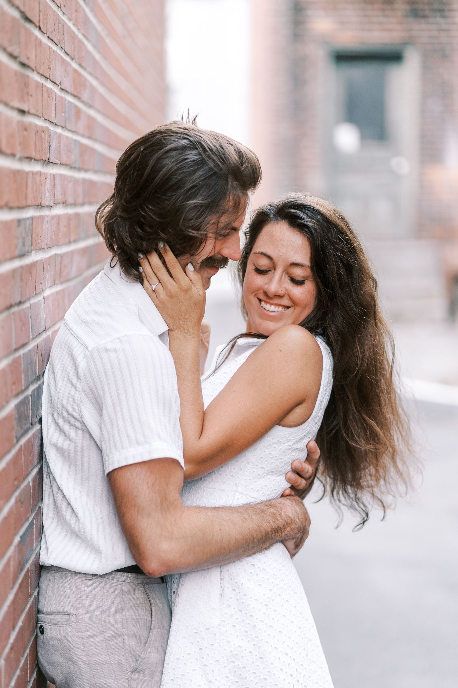 Tender moment shared between couple against urban brick backdrop.