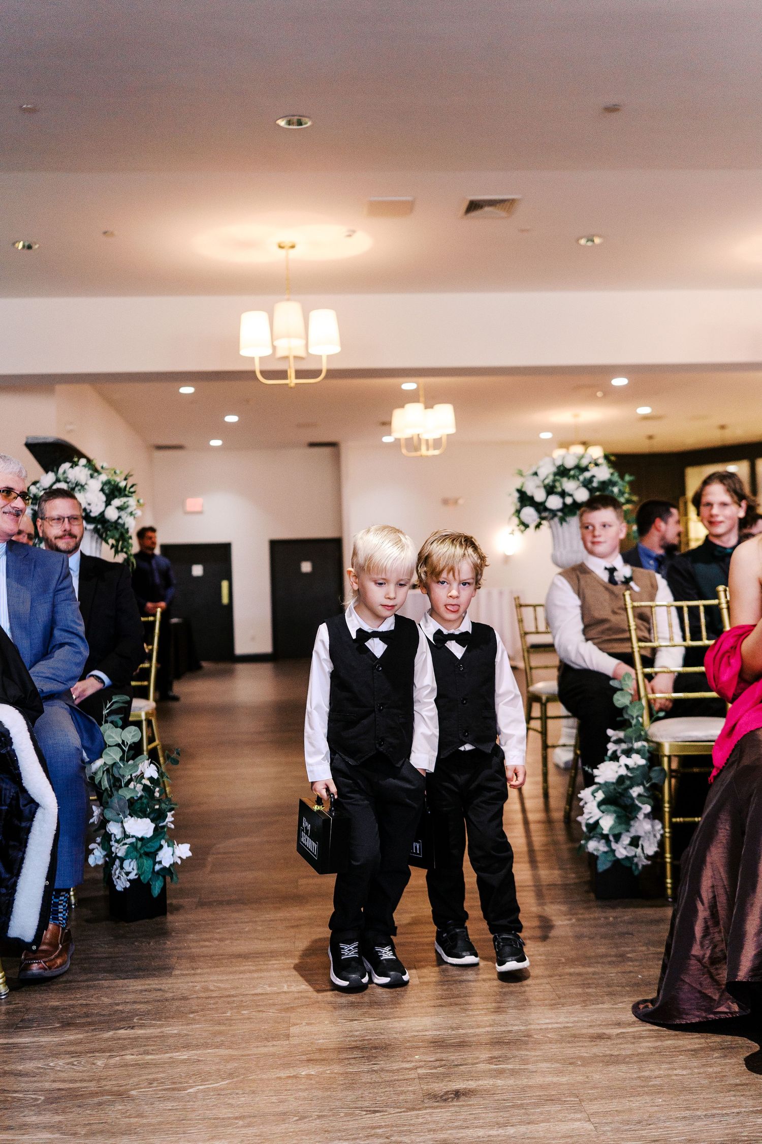 Two young attendants walking down the wedding aisle decorated with floral arrangements.
