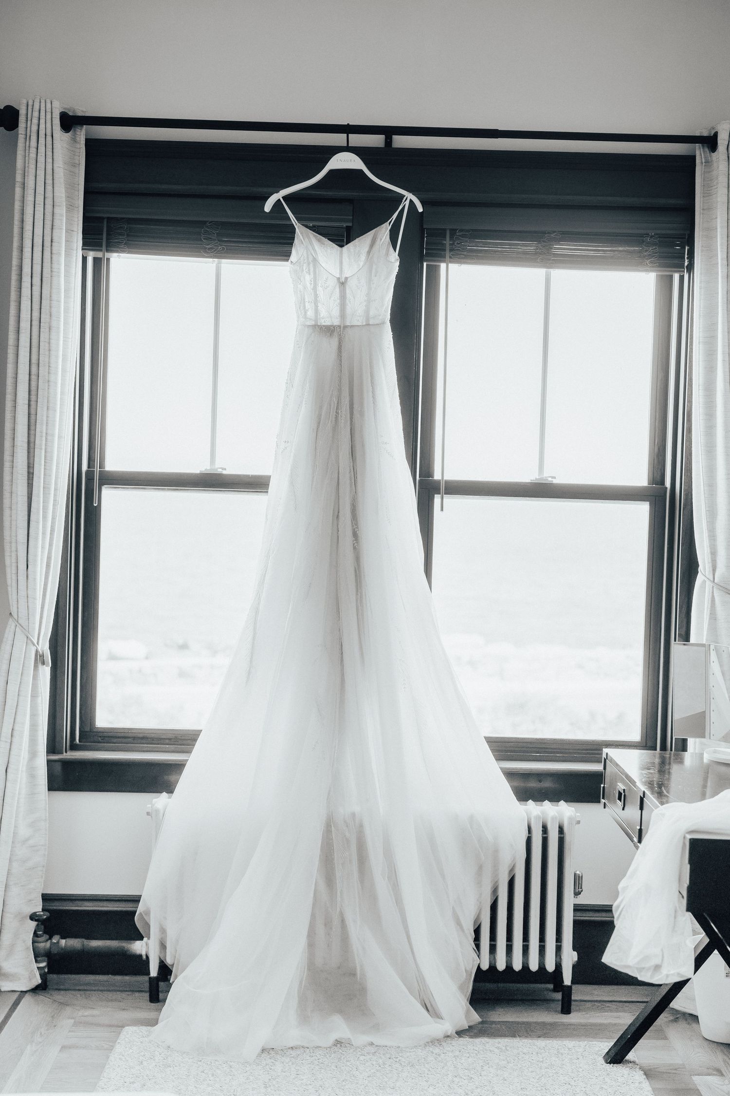 Elegant white wedding dress hanging in window with natural light streaming in.