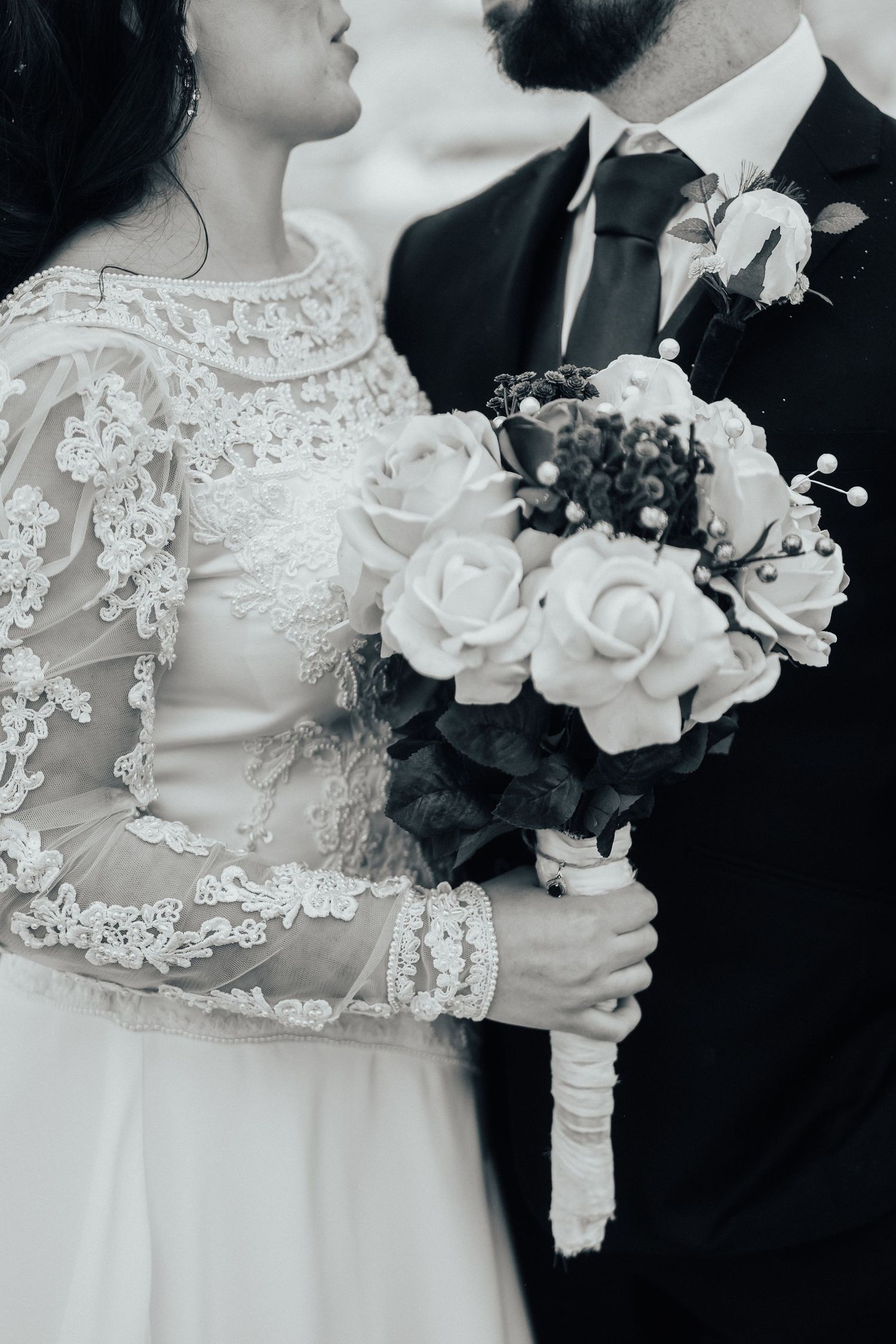 Elegant wedding couple close-up with white lace dress and floral bouquet in black and white.