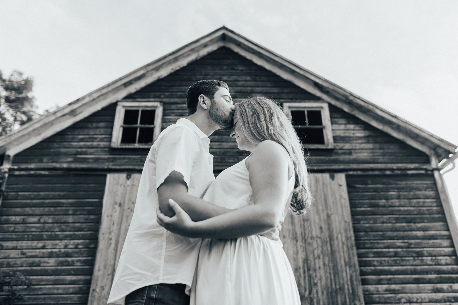 A romantic black and white wedding photo sequence showing tender moments in front of a rustic wooden barn.