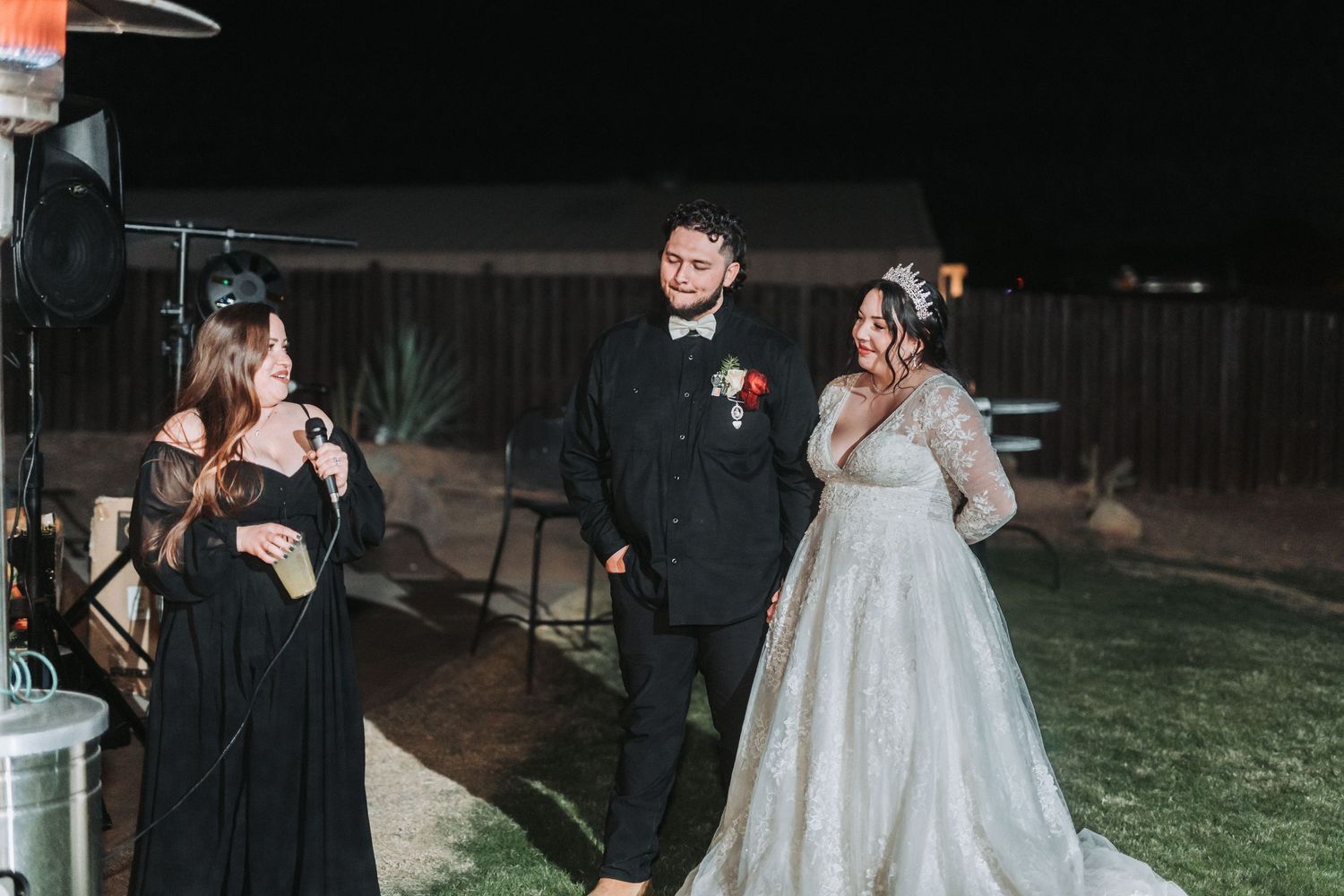A wedding party in formal attire sharing a lighthearted moment together on a dark evening outdoors.