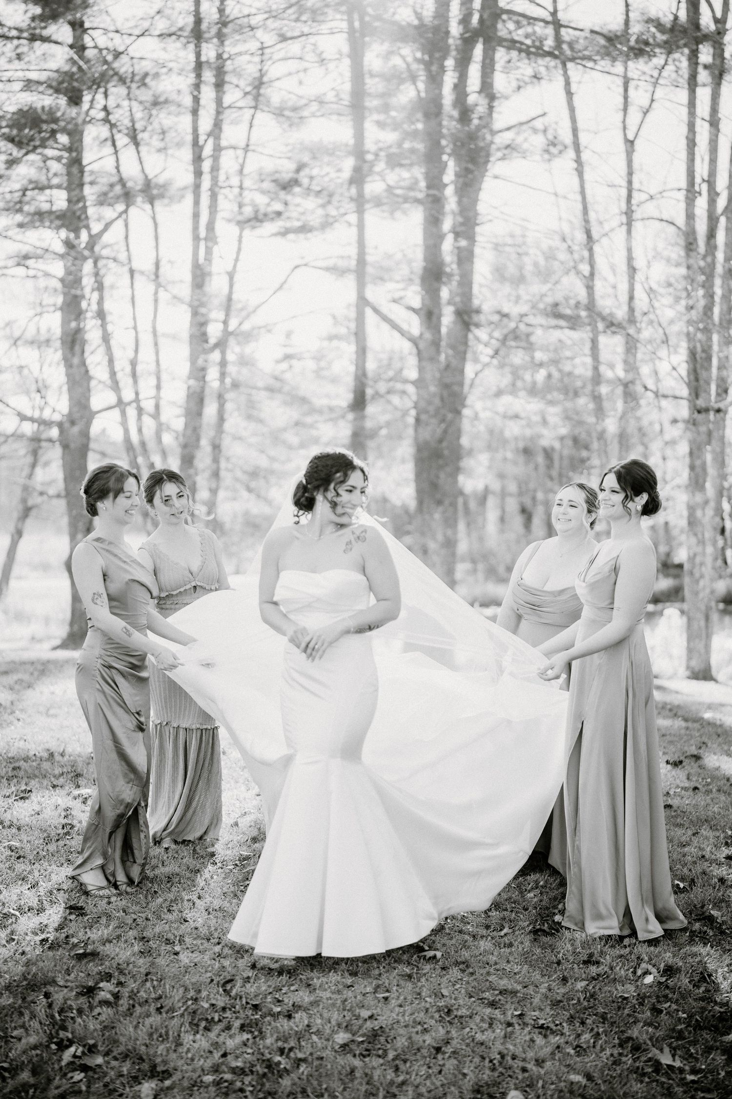 A sequence of black and white photos showing bridesmaids helping adjust a flowing white wedding dress in a forest setting.