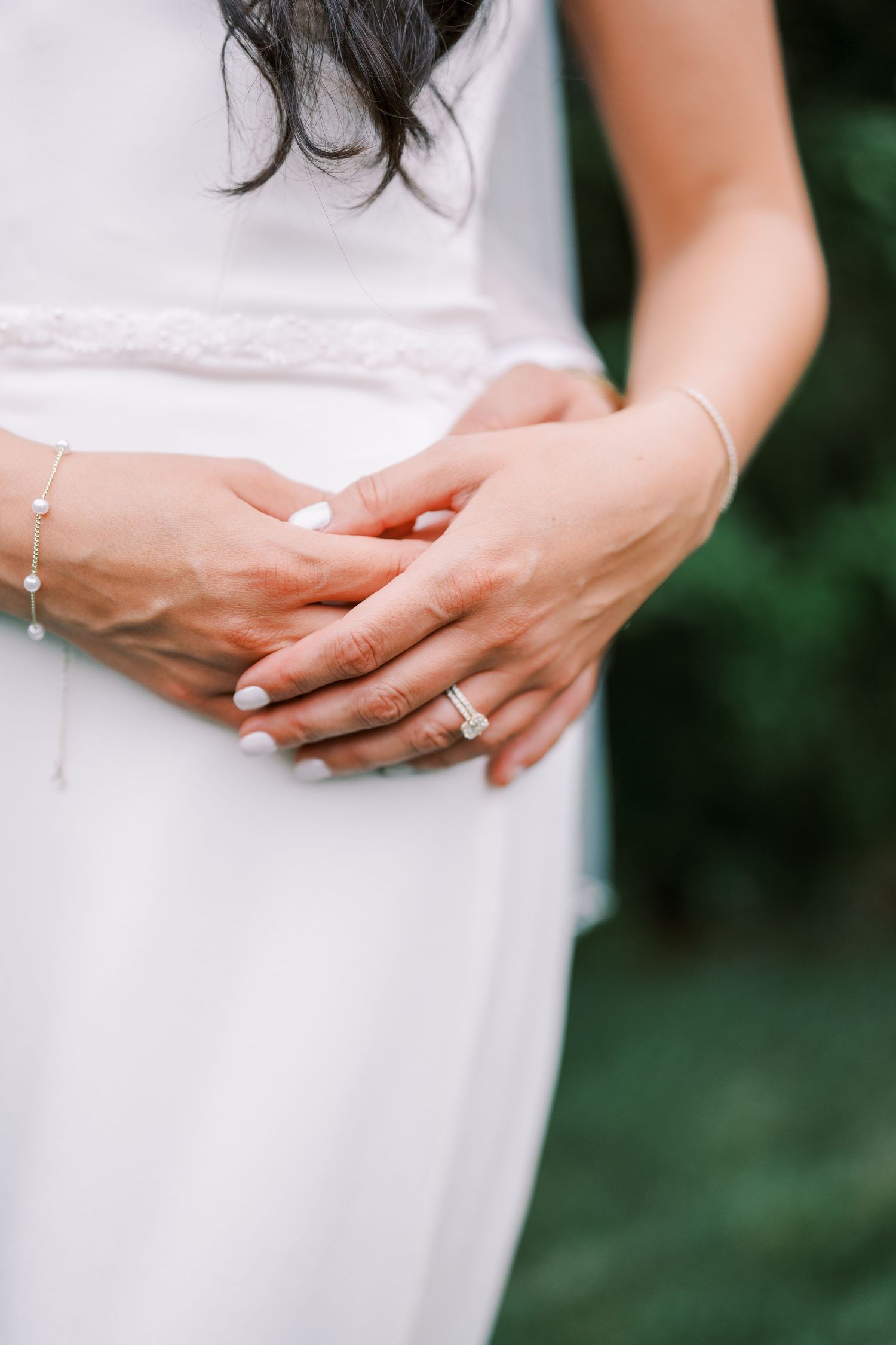 Close-up of hands showing off an engagement ring on a white dress with soft natural lighting.