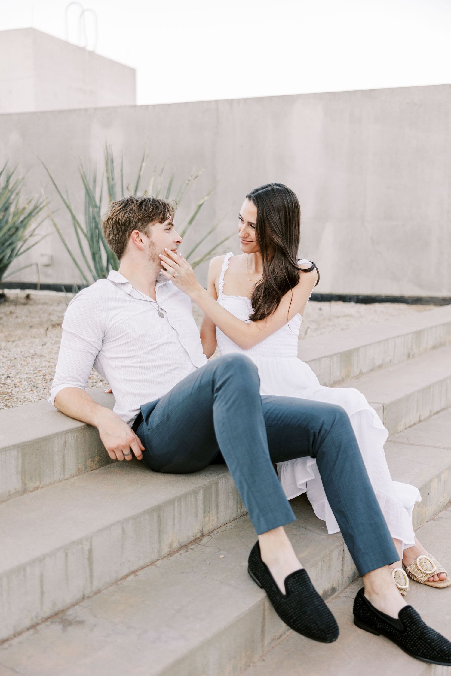 Couple in casual attire sitting on white concrete steps in modern setting.
