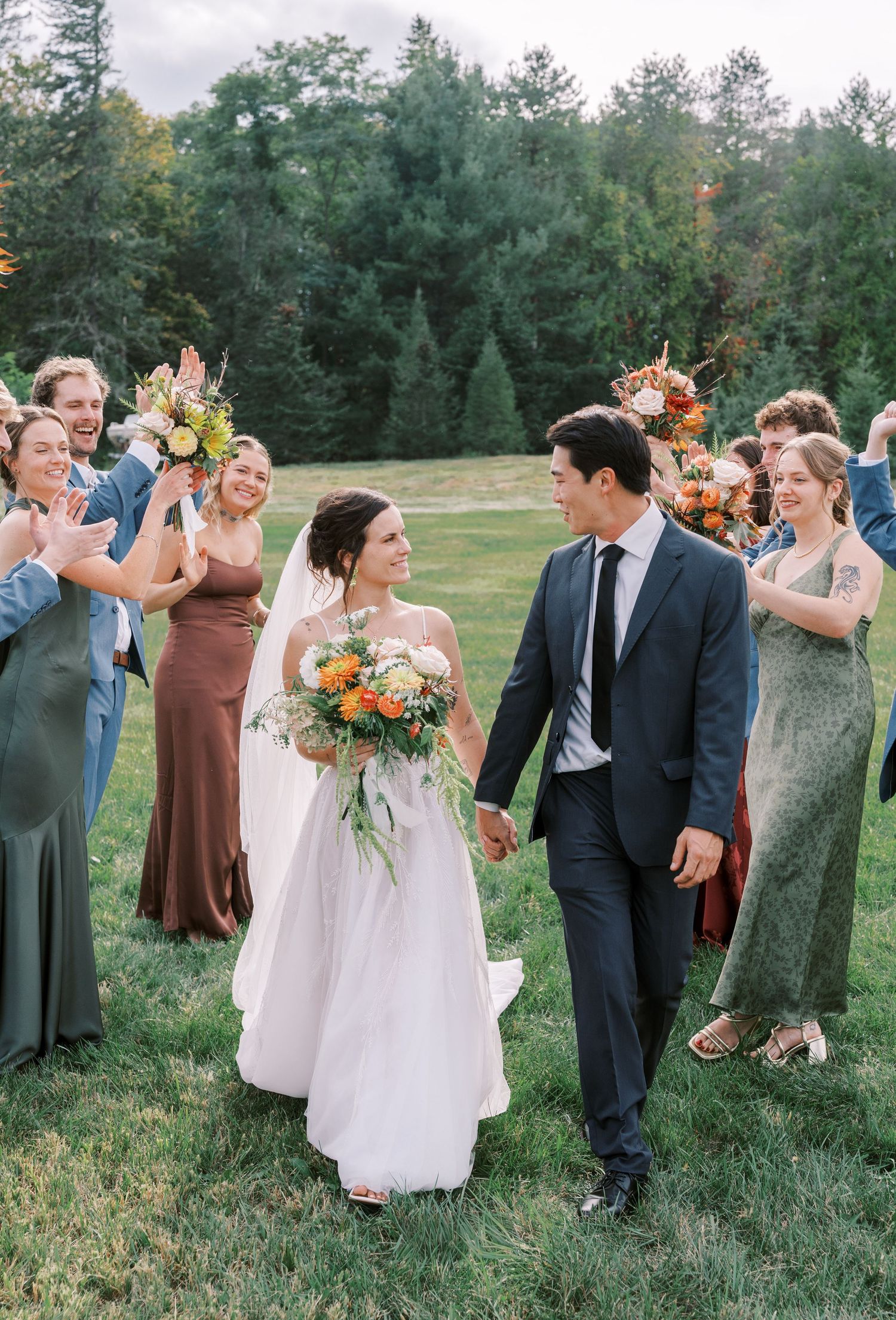 Wedding party celebrates on a lush green lawn with pine trees in the background.