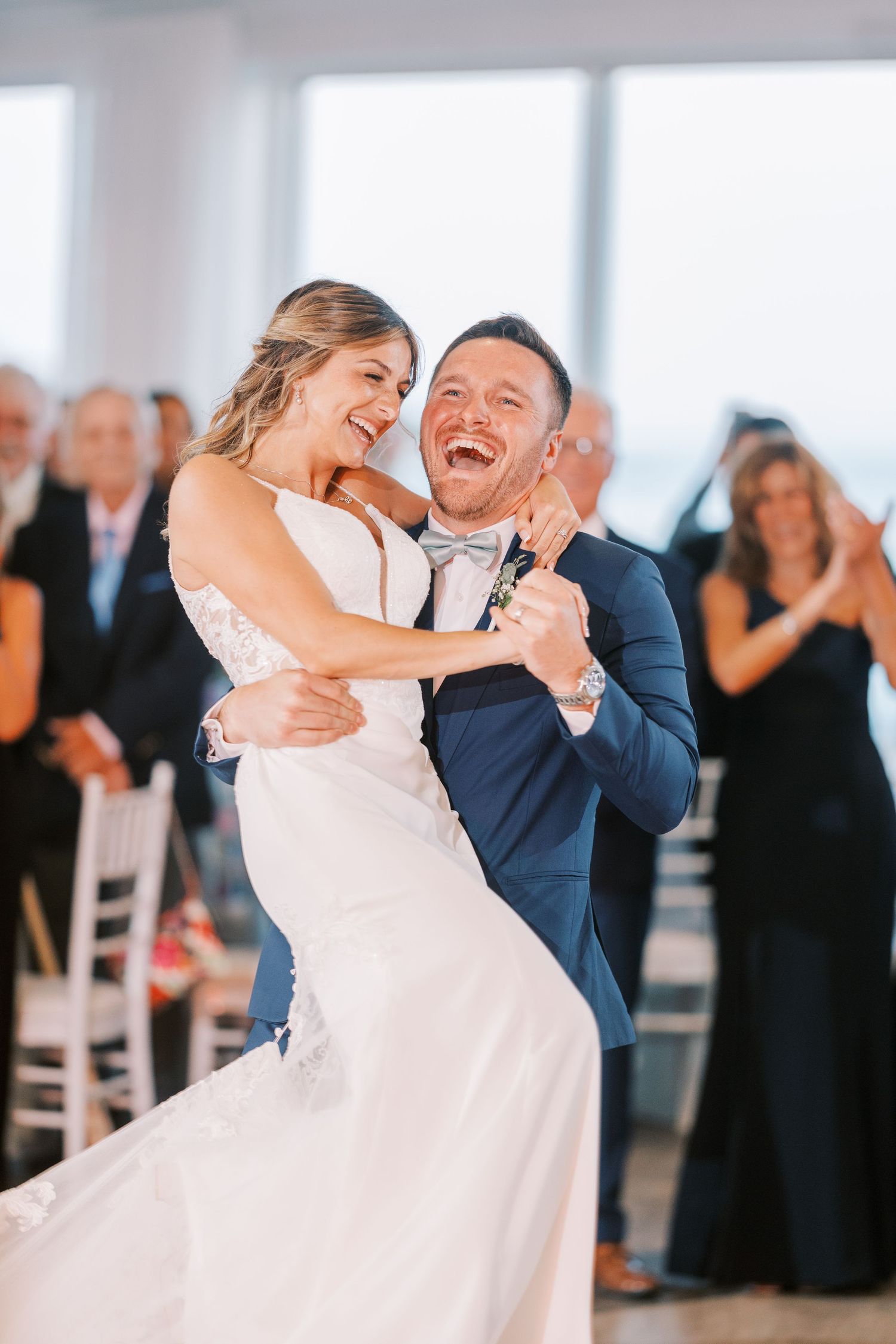 A bride and groom share a joyful dance during their wedding reception as guests look on in the background.