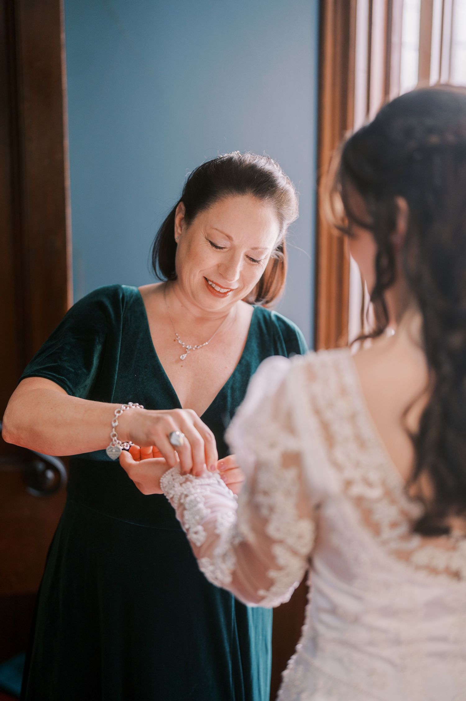 Two women share a joyful moment as they prepare for a wedding ceremony in a sunlit room.