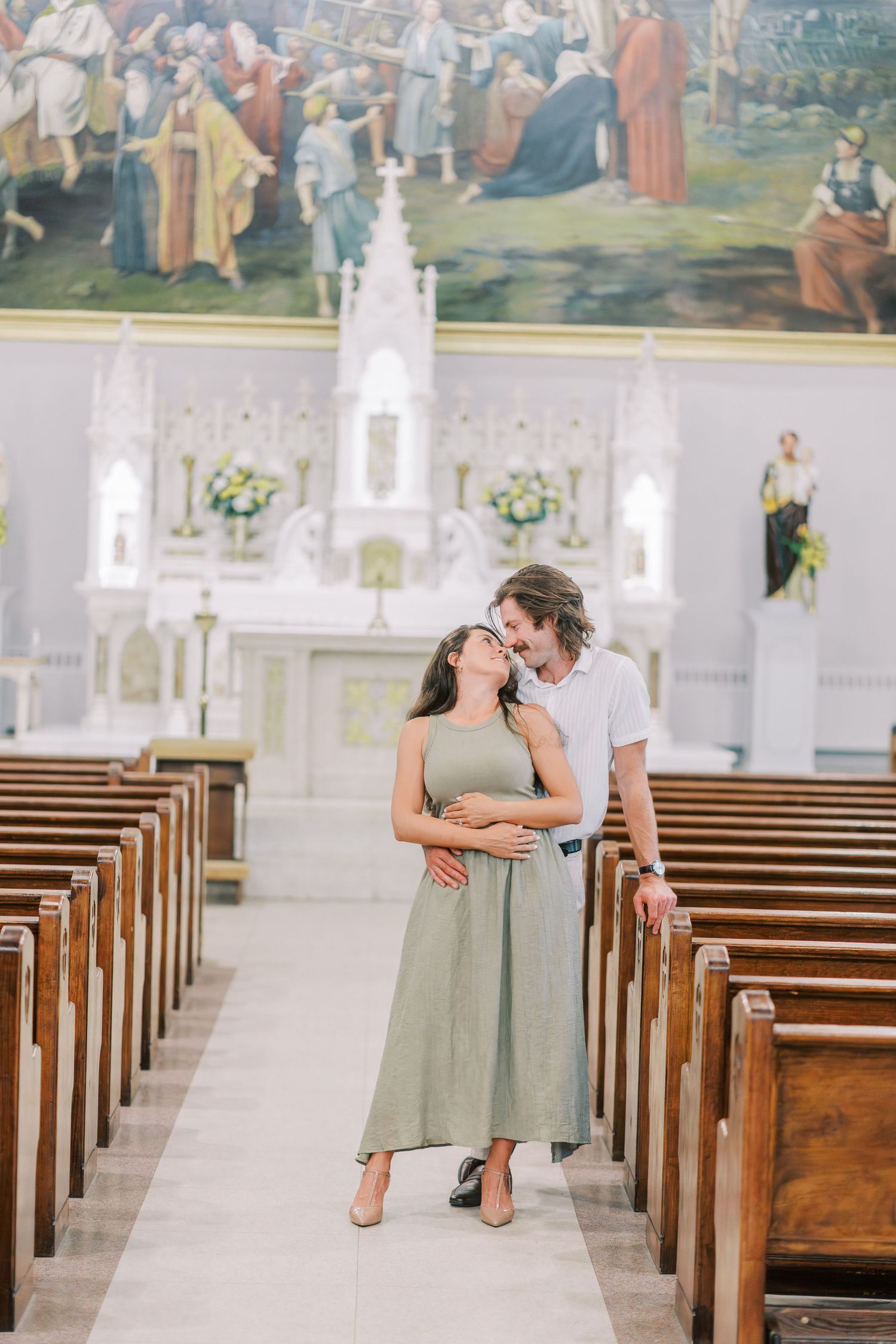 Couple sharing an intimate moment in an elegant church with wooden pews and ornate altar.