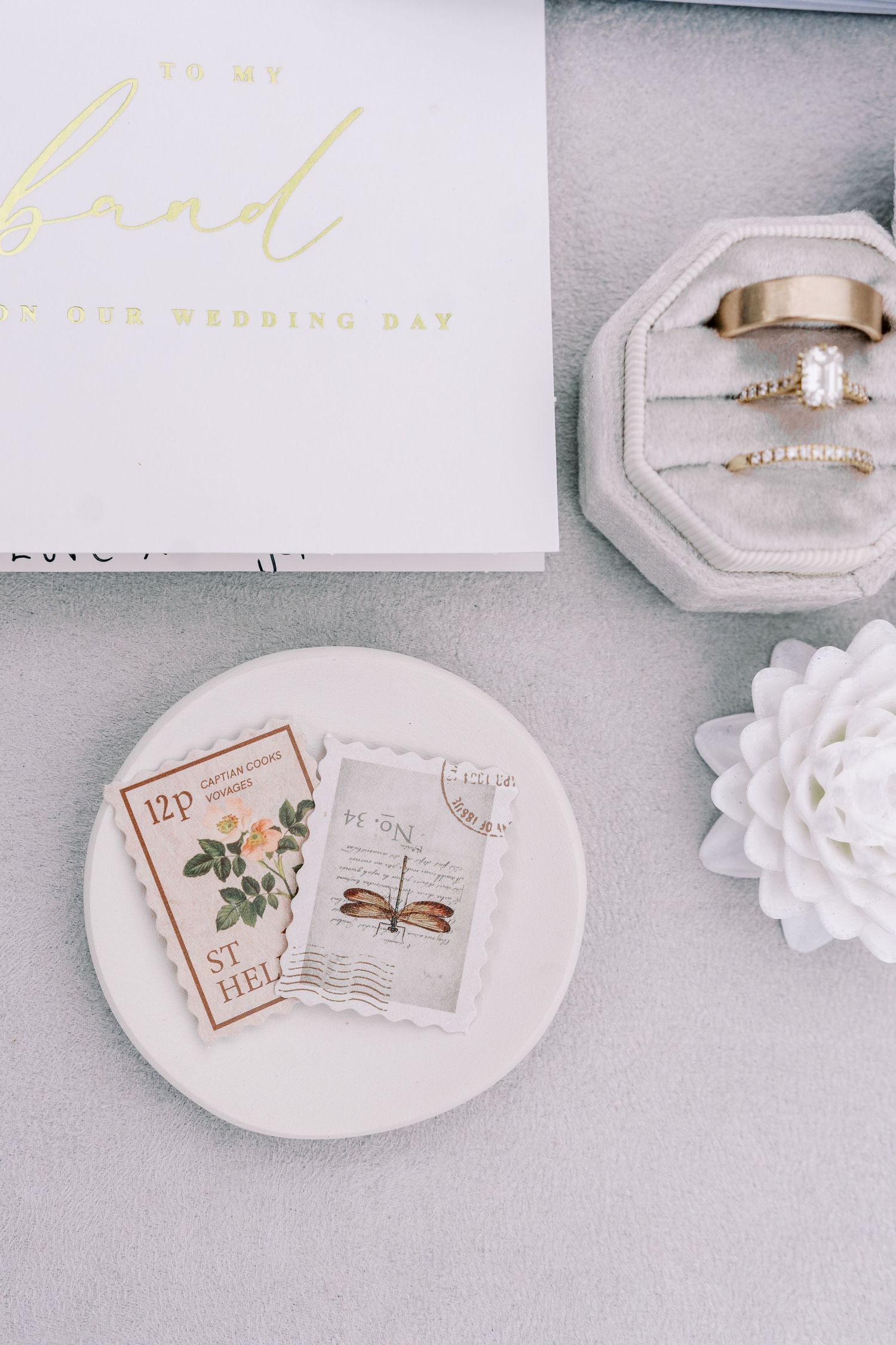 Wedding details including rings, invitation cards, and decorative elements arranged on a light gray surface.