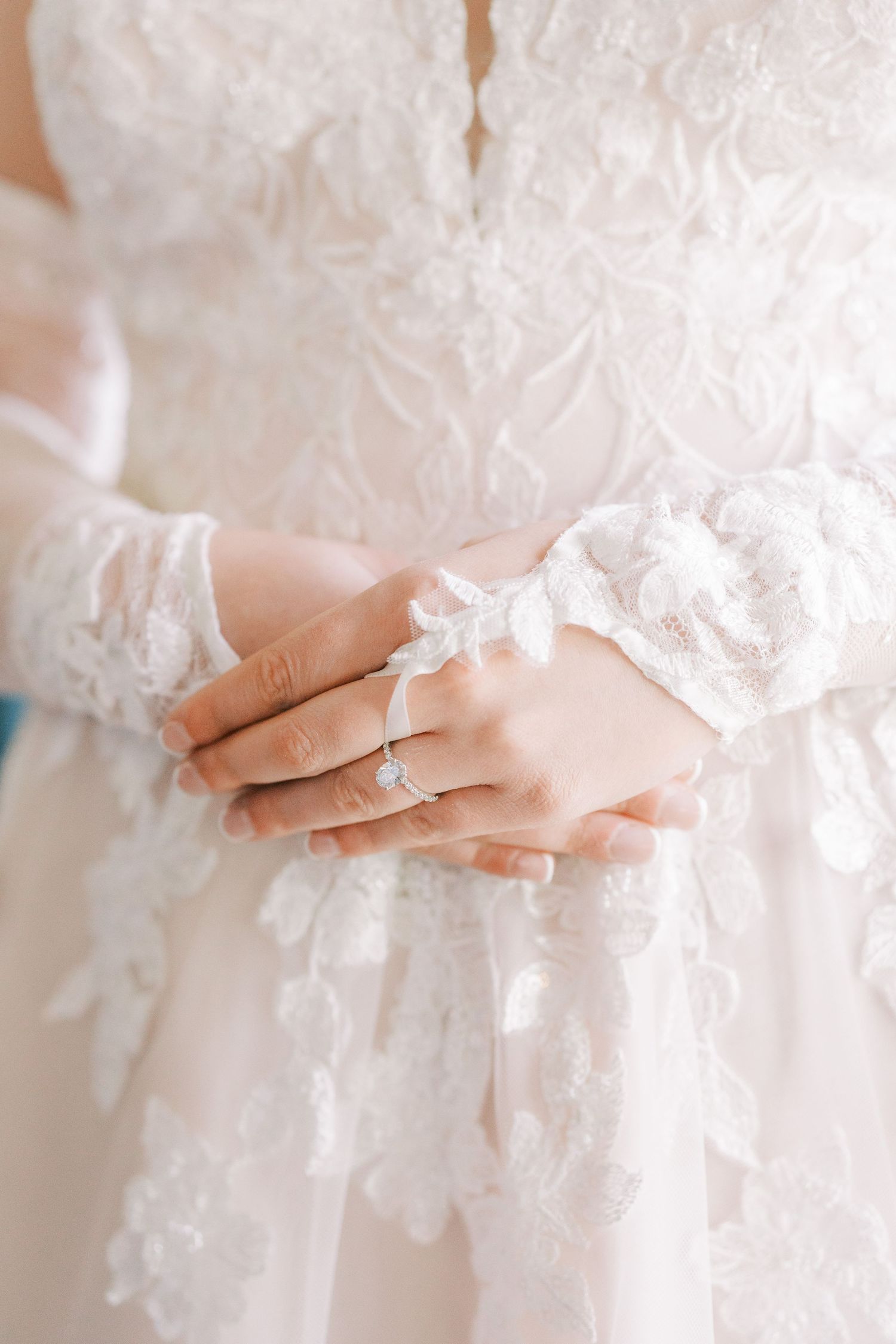 Close-up details of delicate white lace and fabric on a wedding dress with soft ethereal lighting.