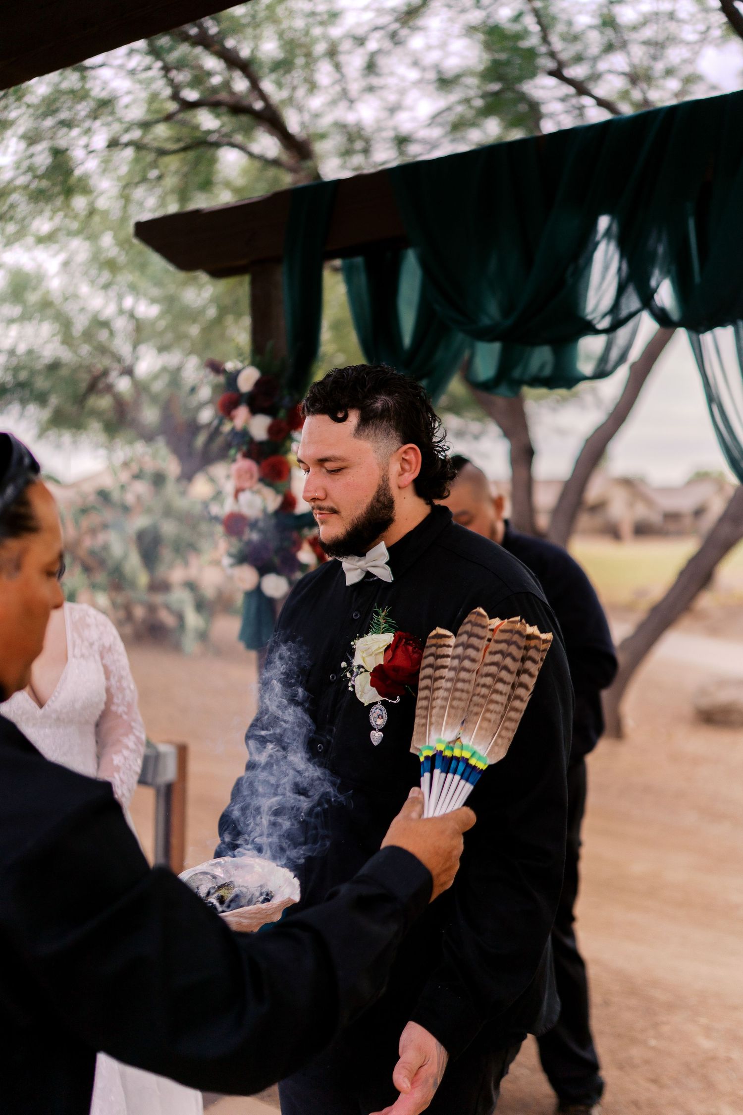 A spiritual ceremony takes place outdoors as smoke and feathers are used in a cleansing ritual under a canopy.