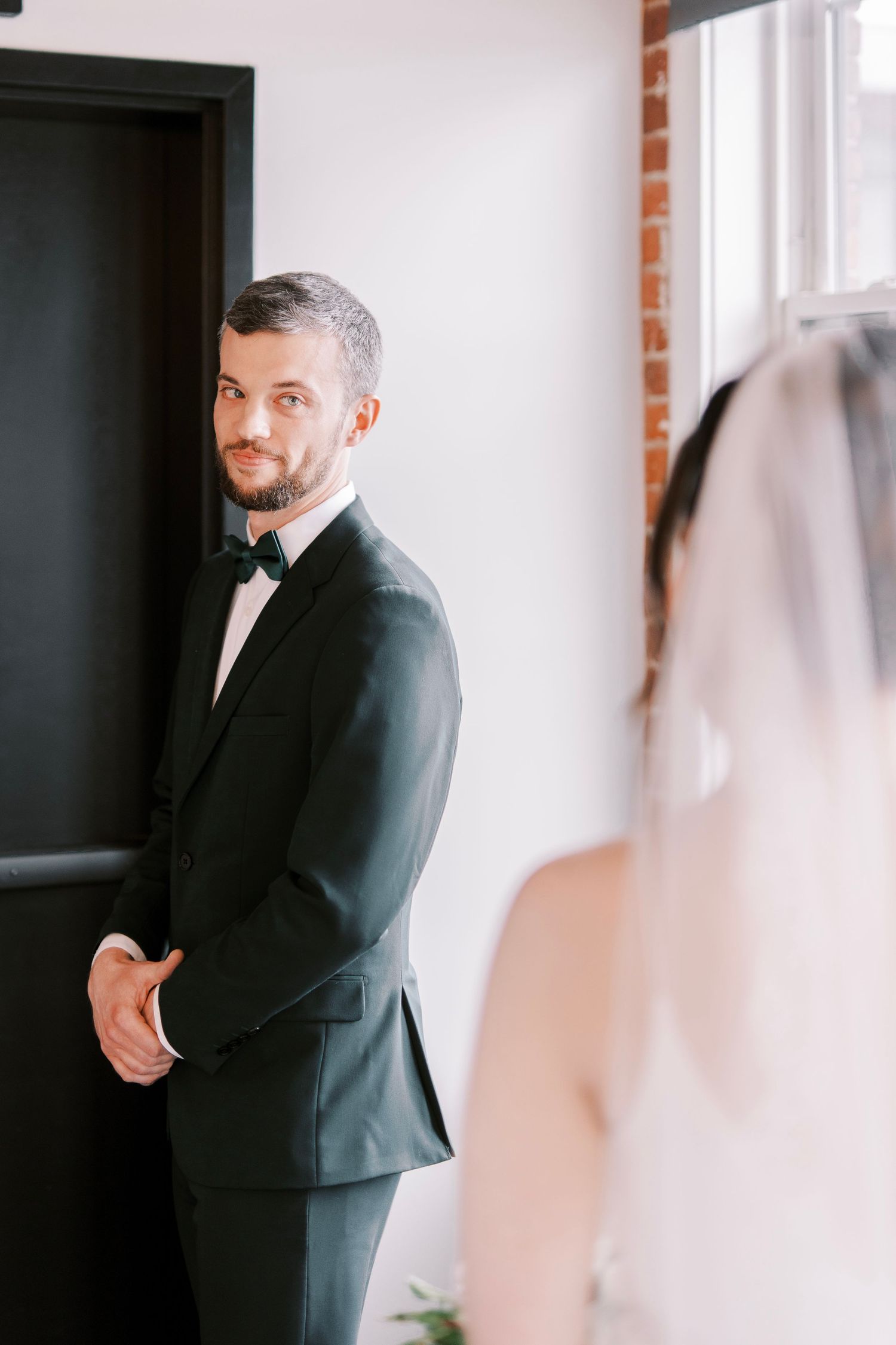A first look wedding moment captured in an industrial-style hallway with brick walls and natural light.